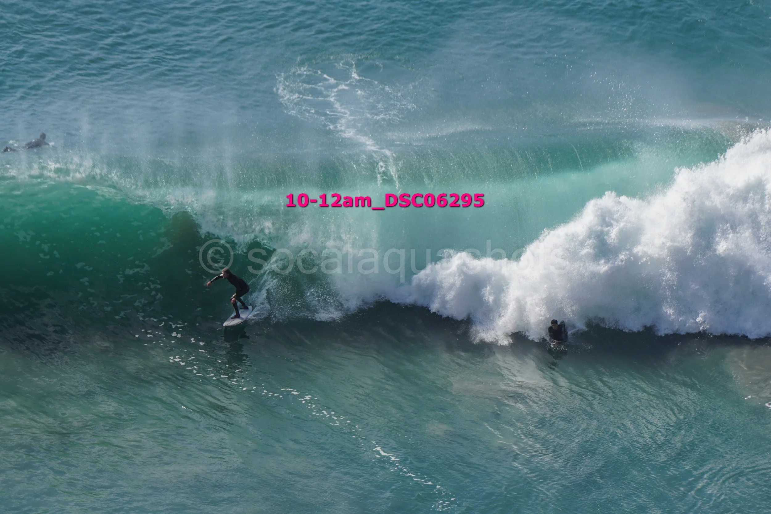 Surfer riding a large wave with photographers capturing the moment in the water.