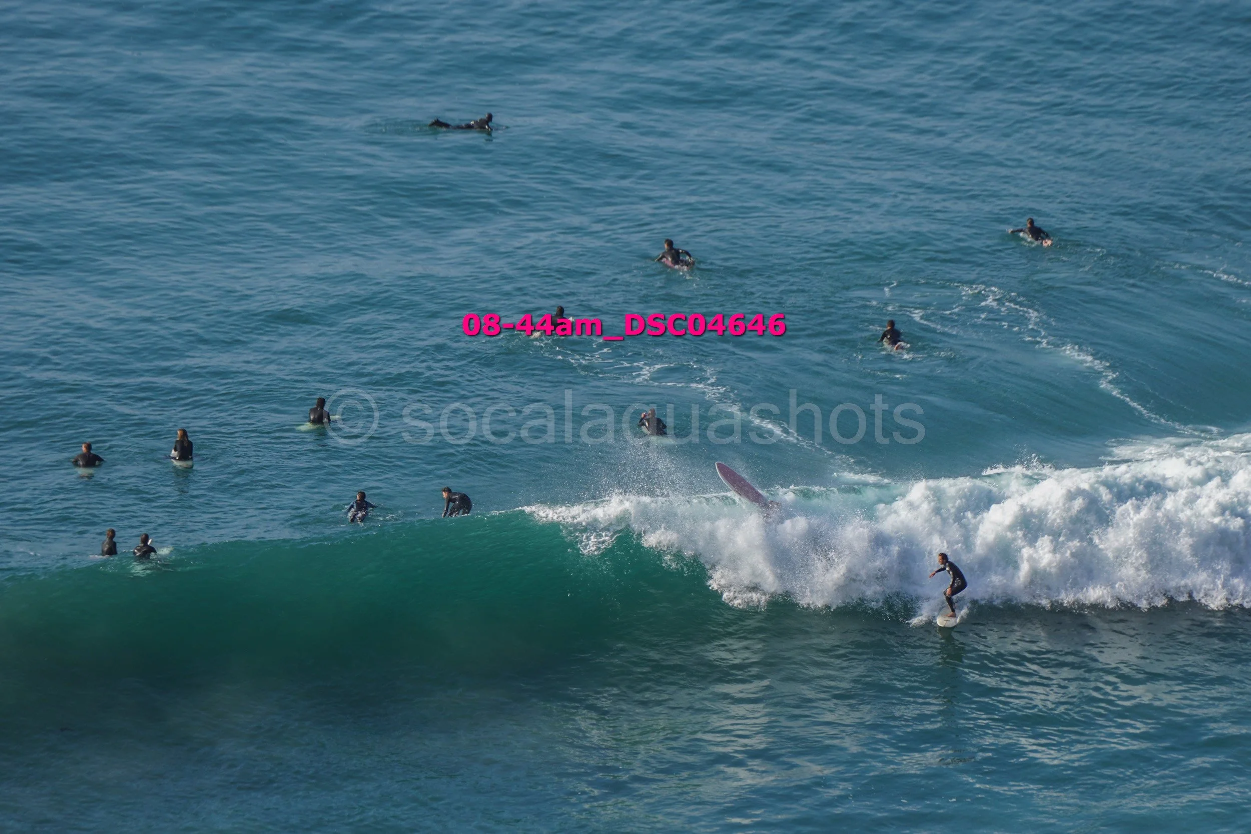 Surfers riding a wave with several people swimming and waiting in the water.