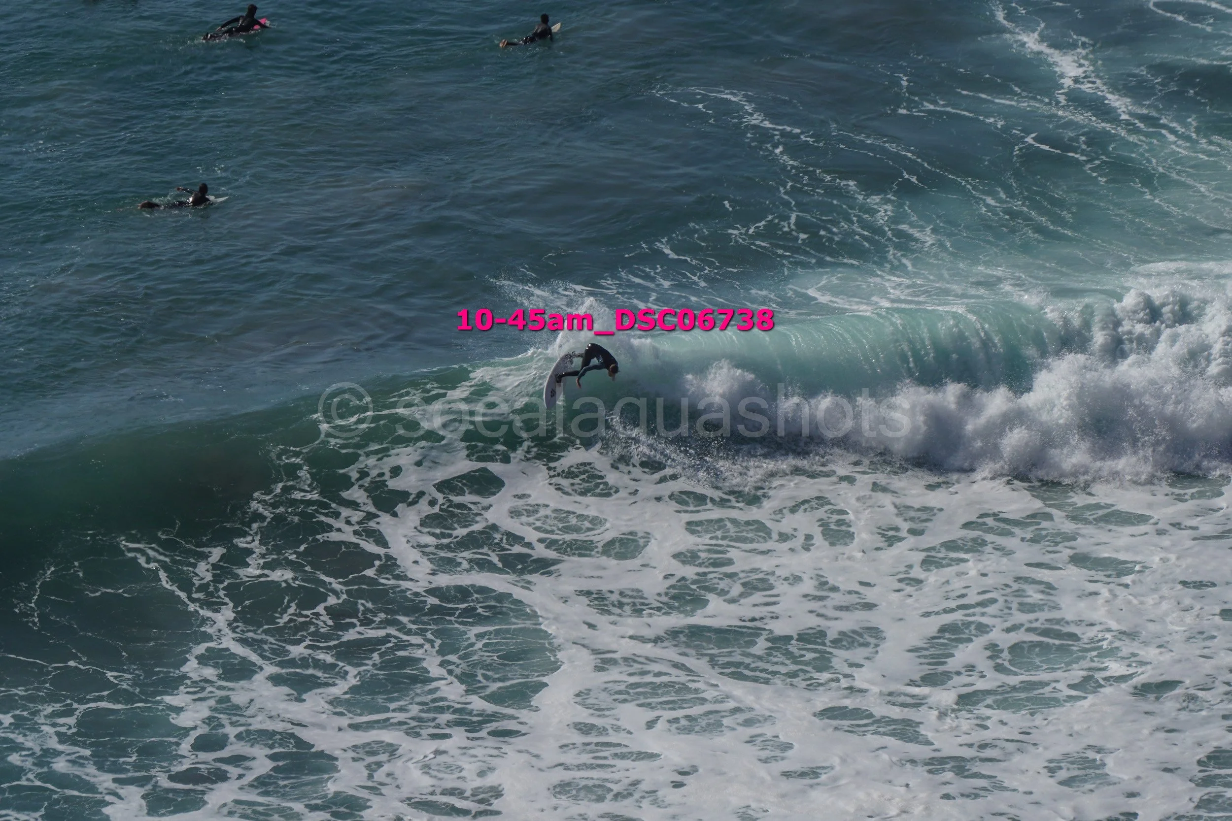 Surfer riding a wave in the ocean with several other surfers in the background.