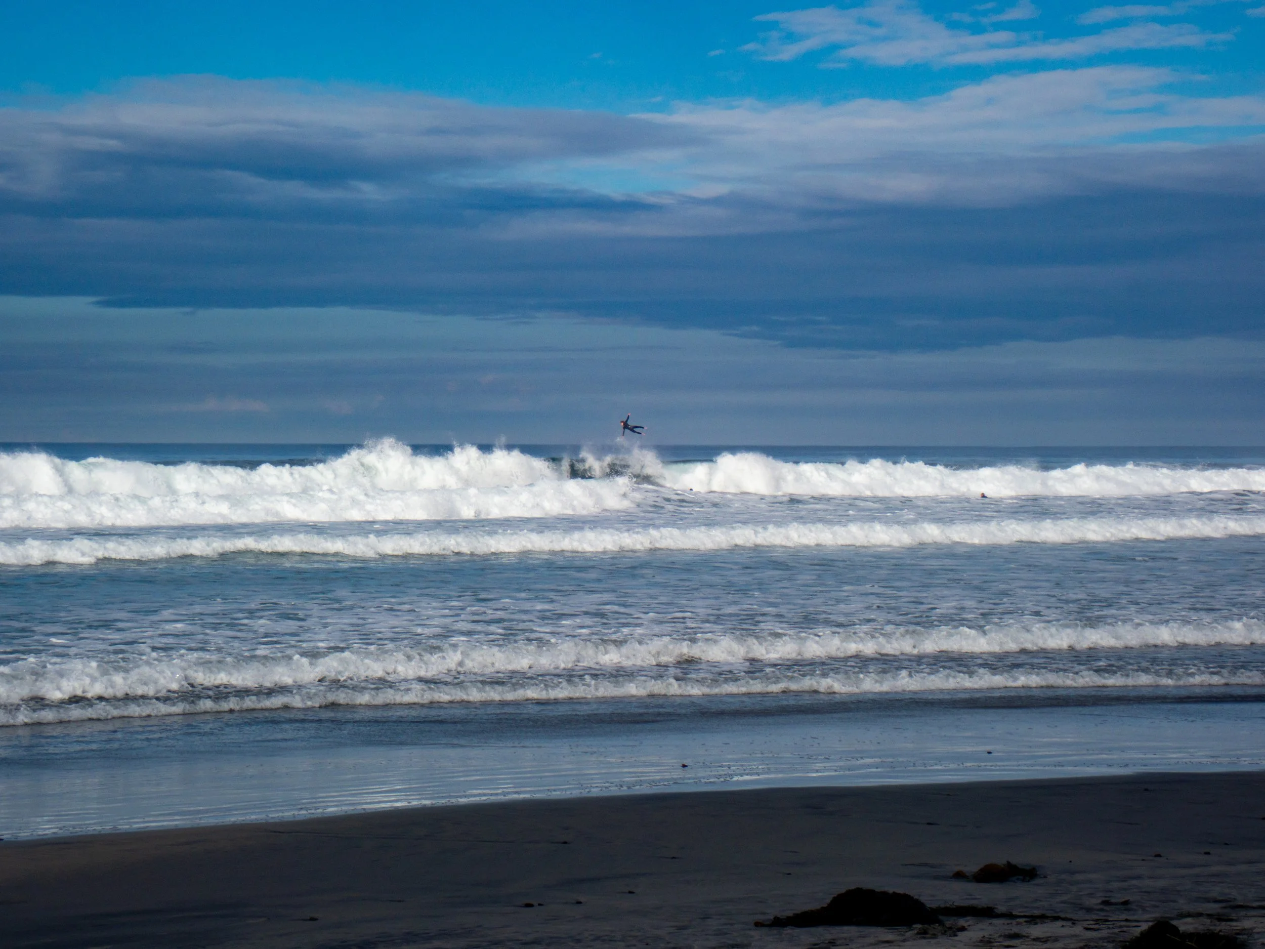 A person kite surfing over ocean waves on a partly cloudy day.