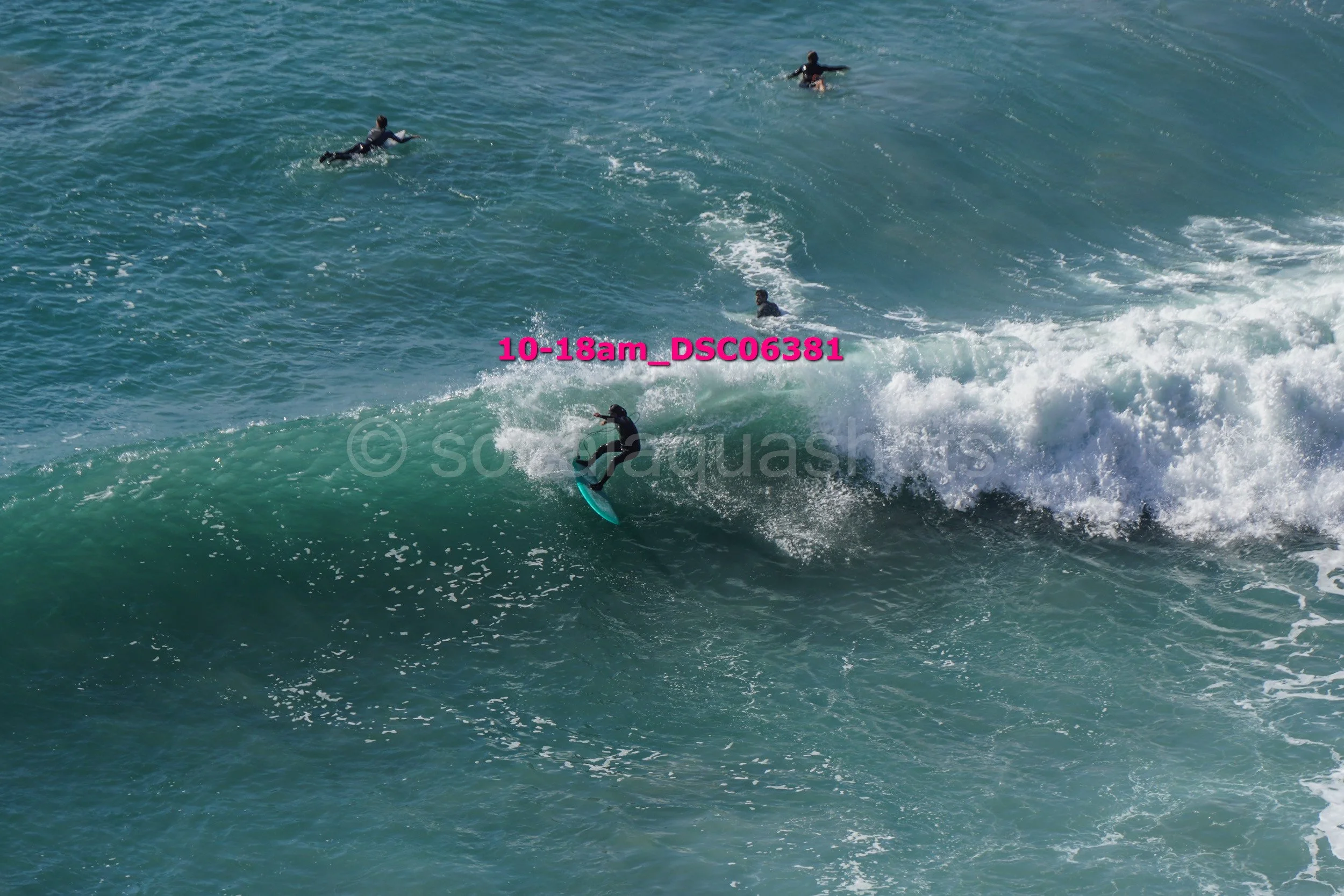 Surfer riding a large wave, with several other surfers in the water in the background.