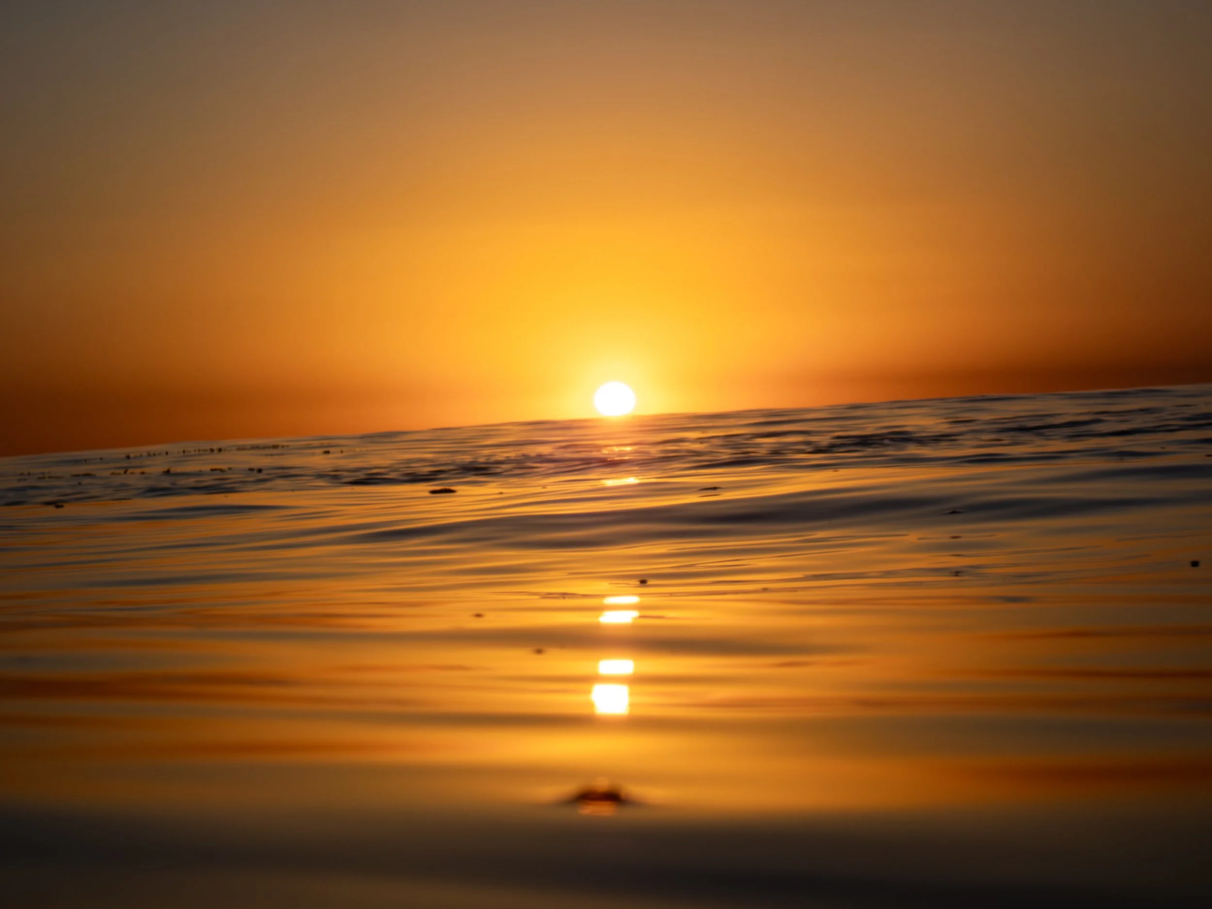 Sunset over the ocean with the sun near the horizon and gentle waves reflecting the orange and yellow colors of the sky.
