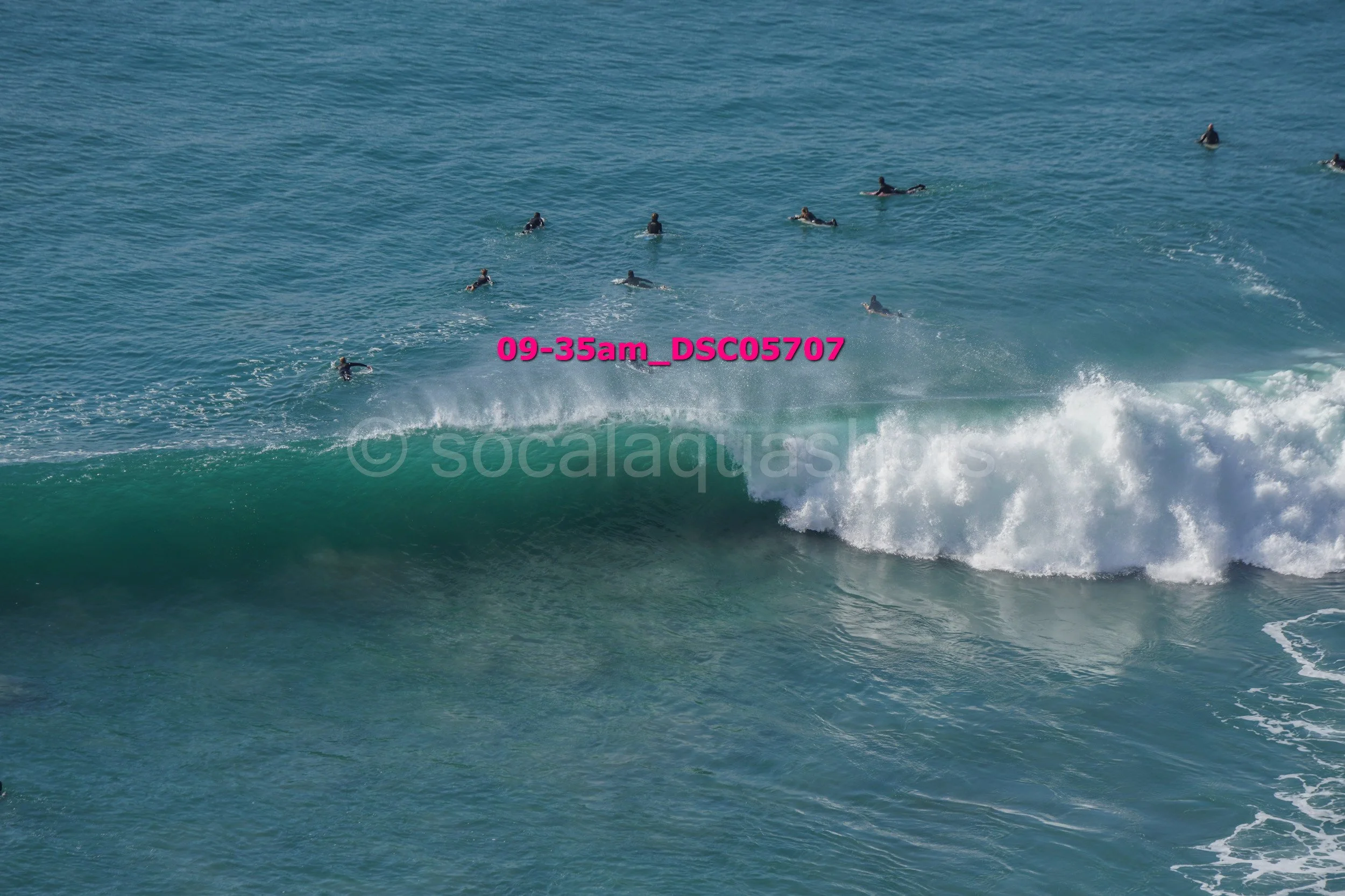 Multiple surfers riding a wave in the ocean on a sunny day.