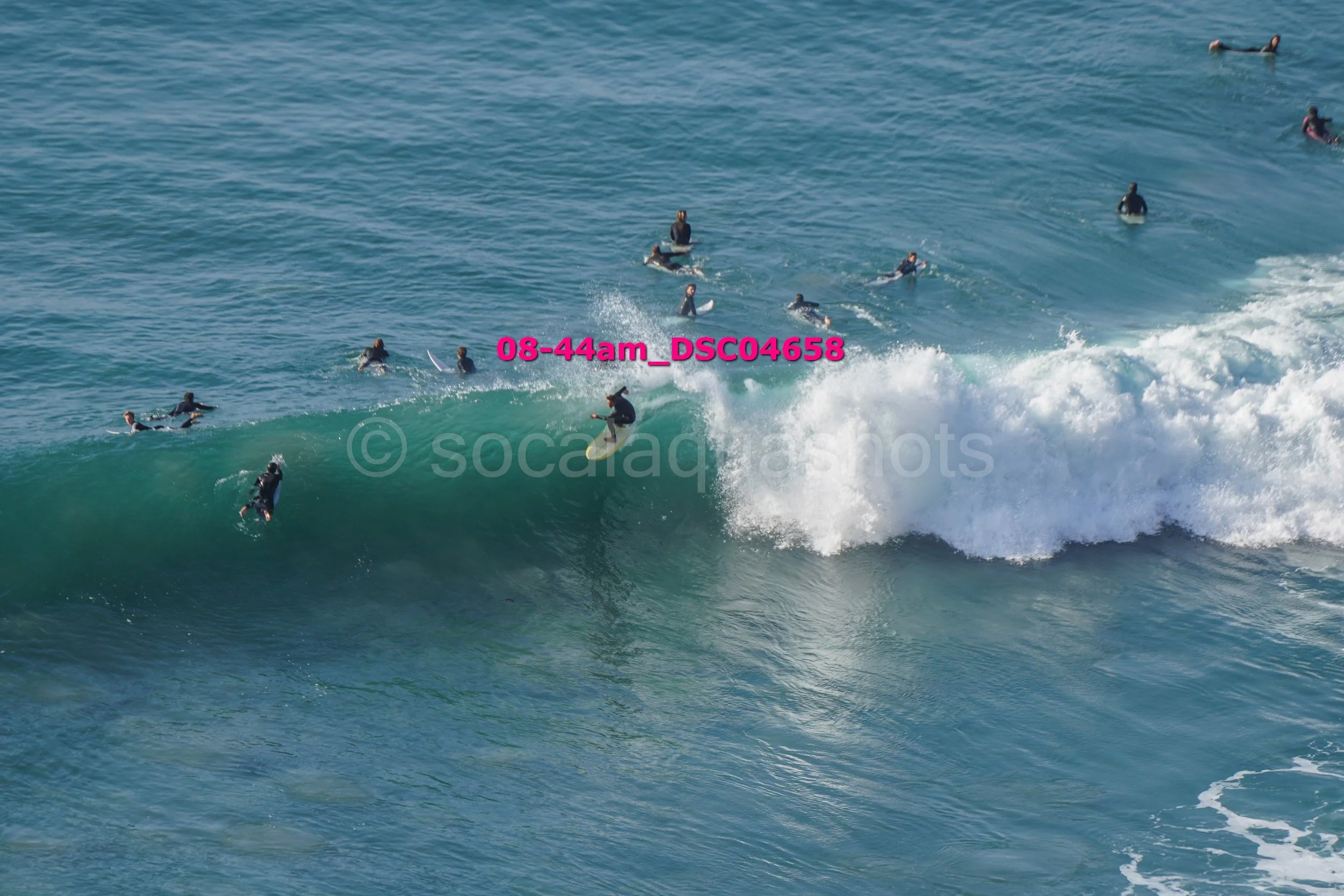 Surfer riding a wave while multiple other surfers and swimmers are in the water around him.