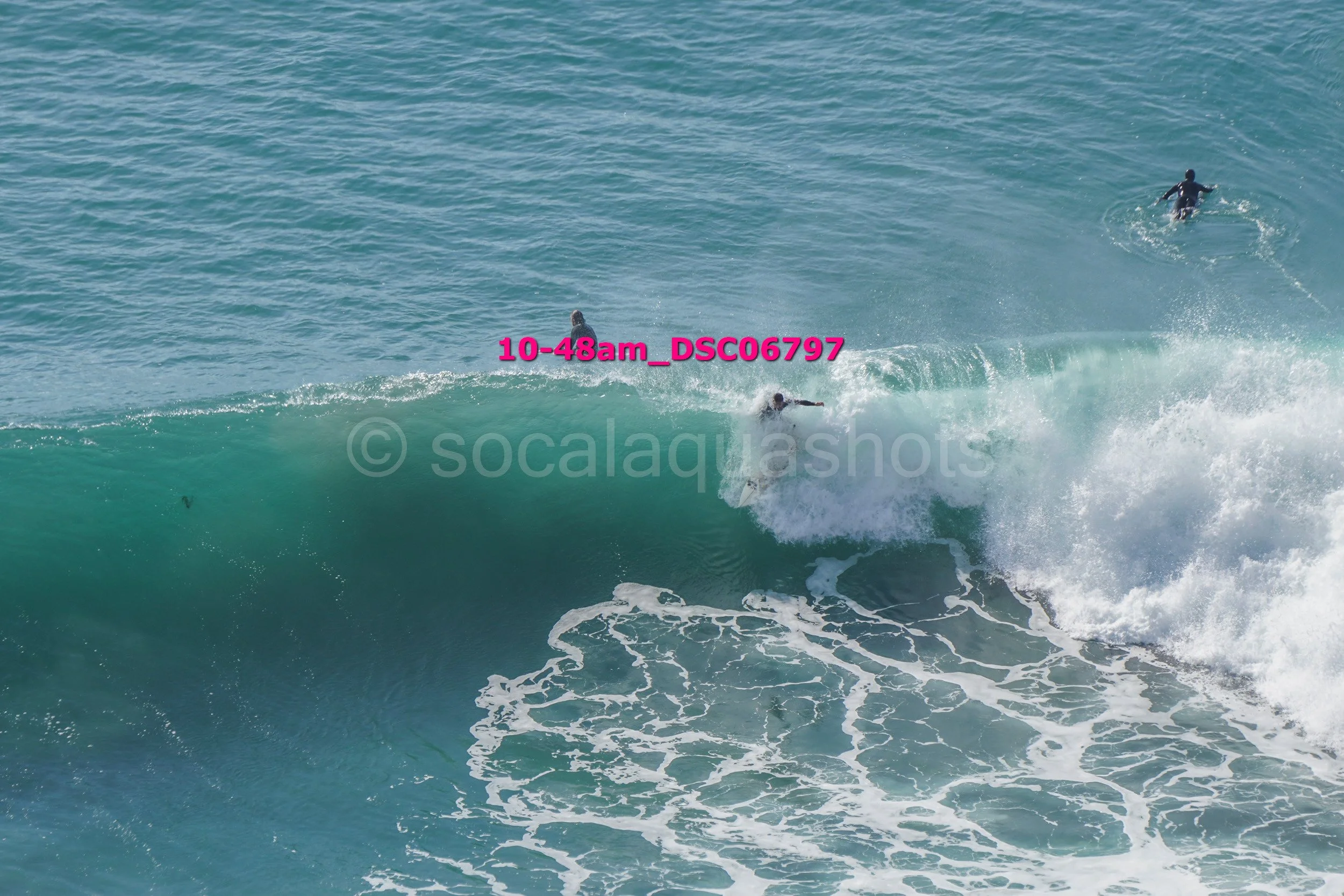 A person surfing on a wave in the ocean with two other surfers in the distance.