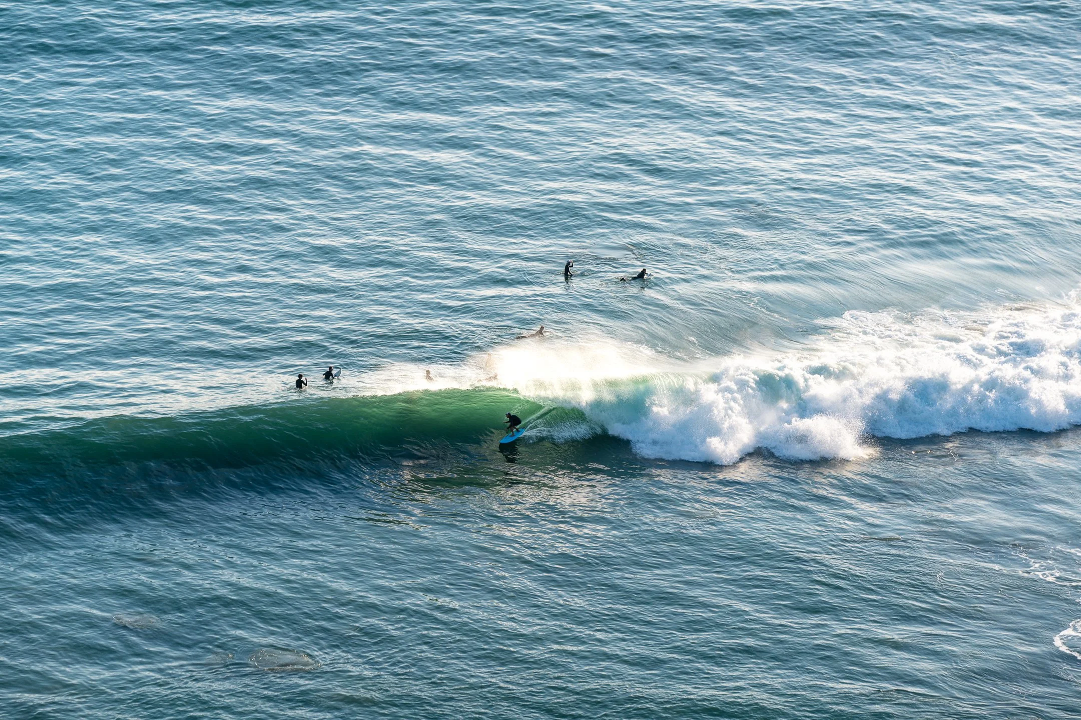 Surfer riding a wave in the ocean with several people swimming nearby.