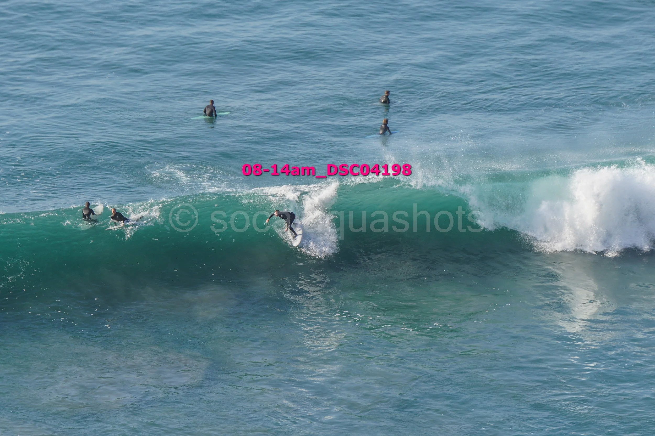 Surfer riding a wave near the shore with several surfers in the water watching or waiting in the distance.