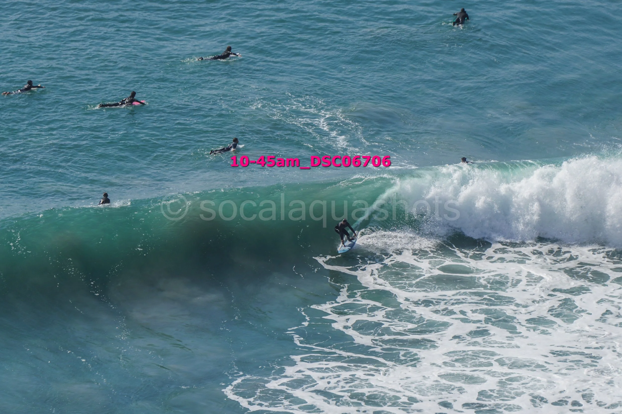 Surfer riding a wave while several other surfers wait in the water nearby.
