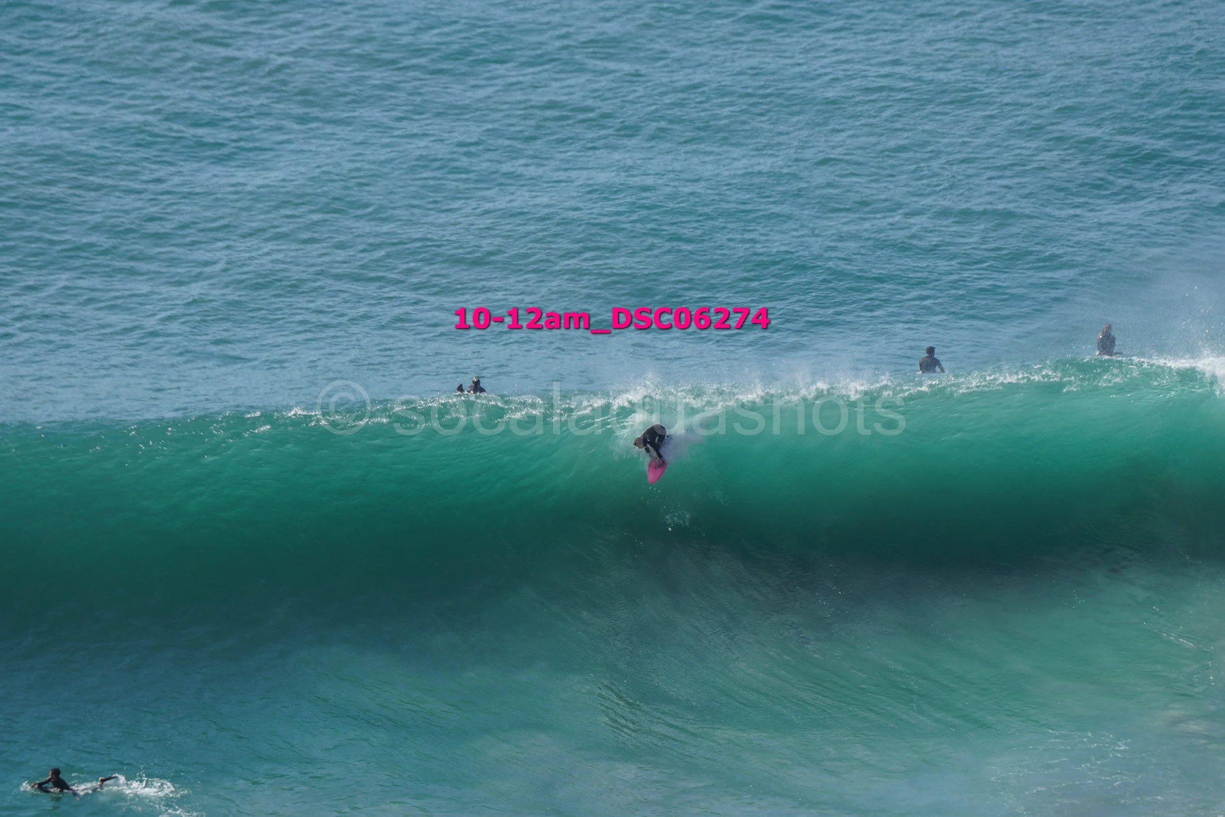 Surfer riding a large wave with other surfers in the background, ocean view.