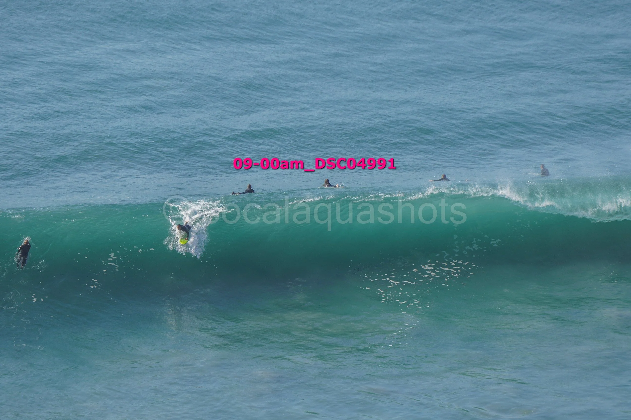 Surfer riding a wave with others swimming and surfing in the background.