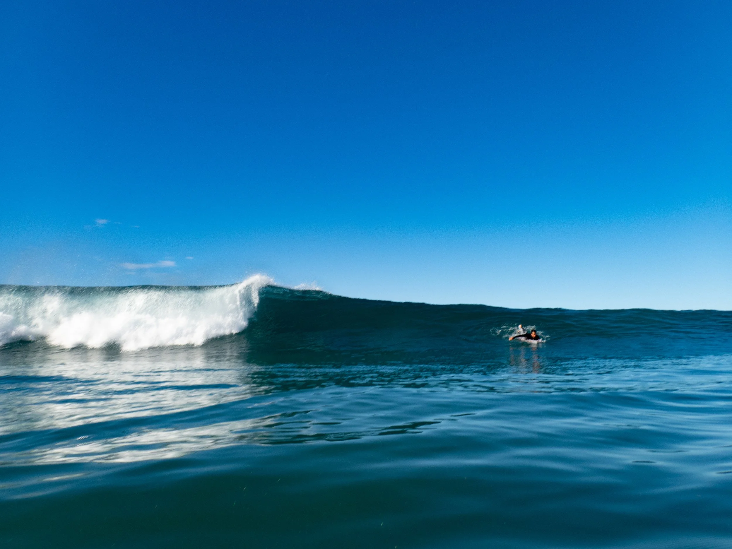 A person riding a wave on a surfboard in the ocean with a clear blue sky overhead.