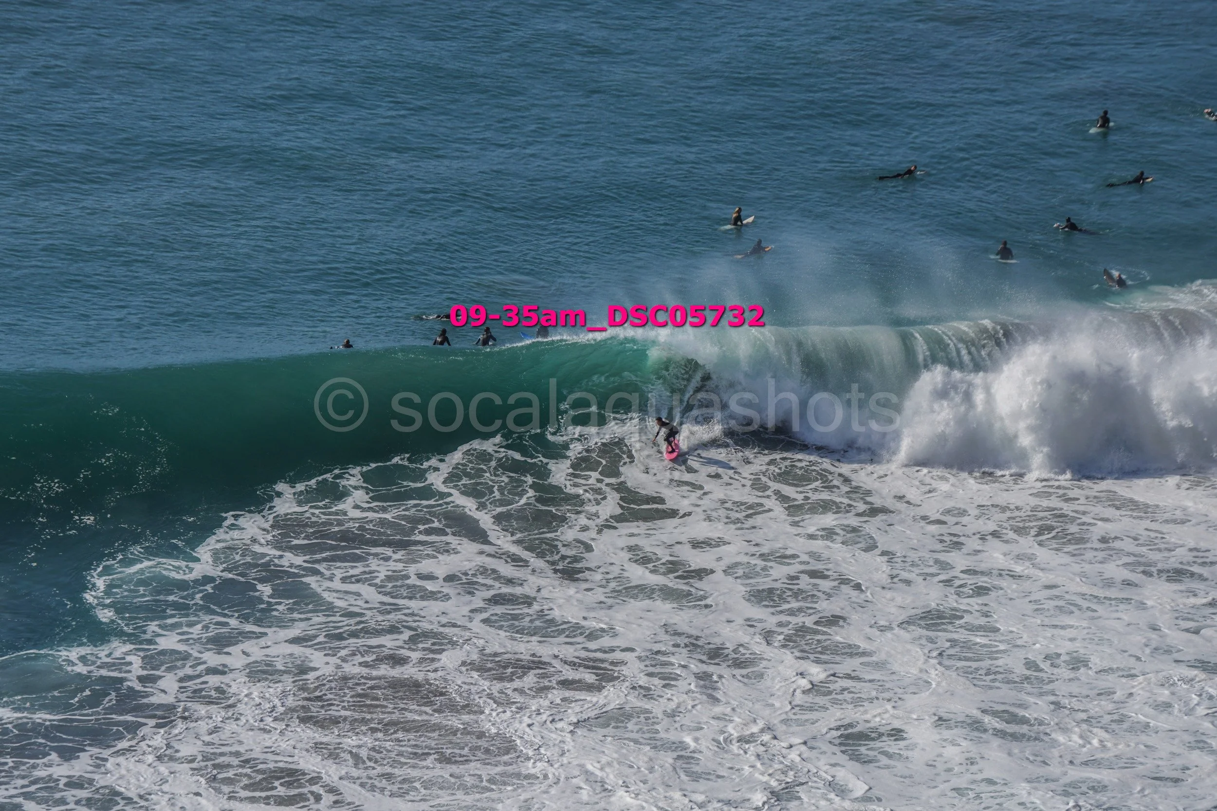 A person surfing on a wave as multiple surfers wait in the water nearby.