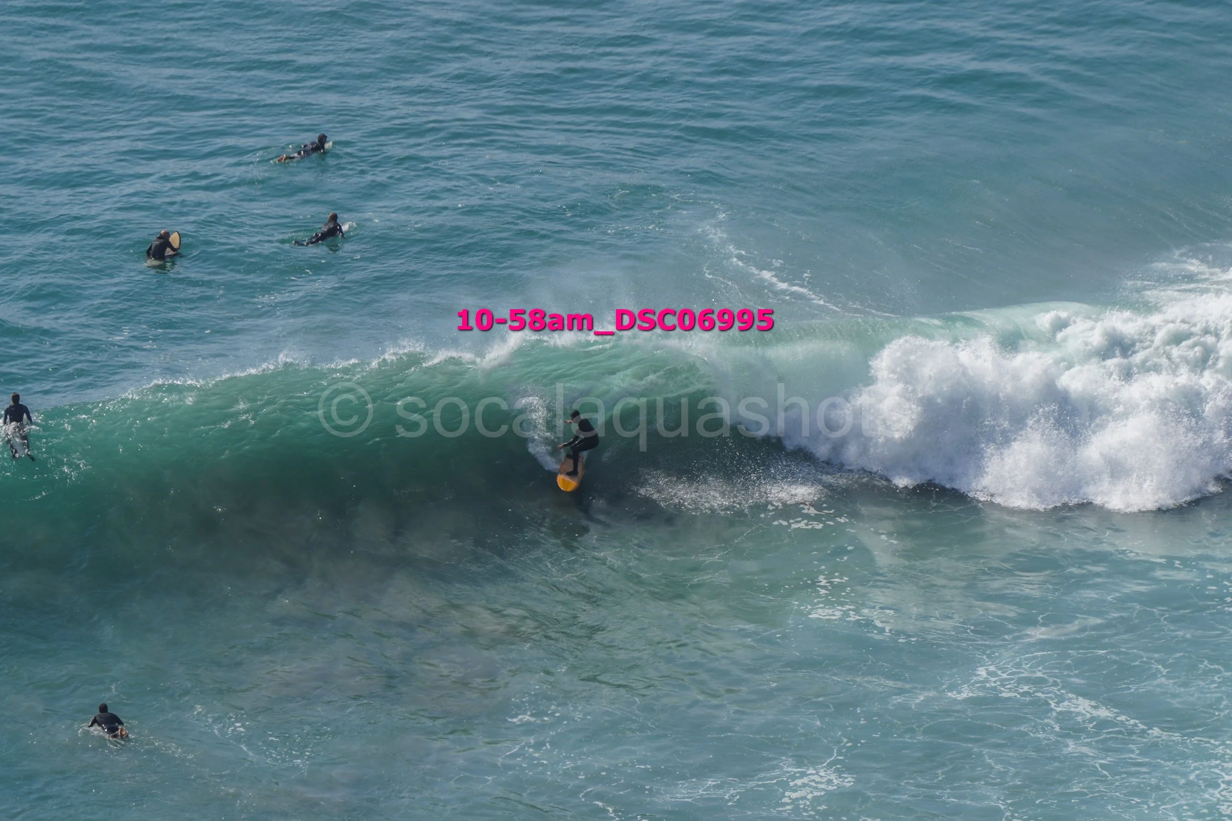 Surfer riding a wave with several other surfers in the water nearby.