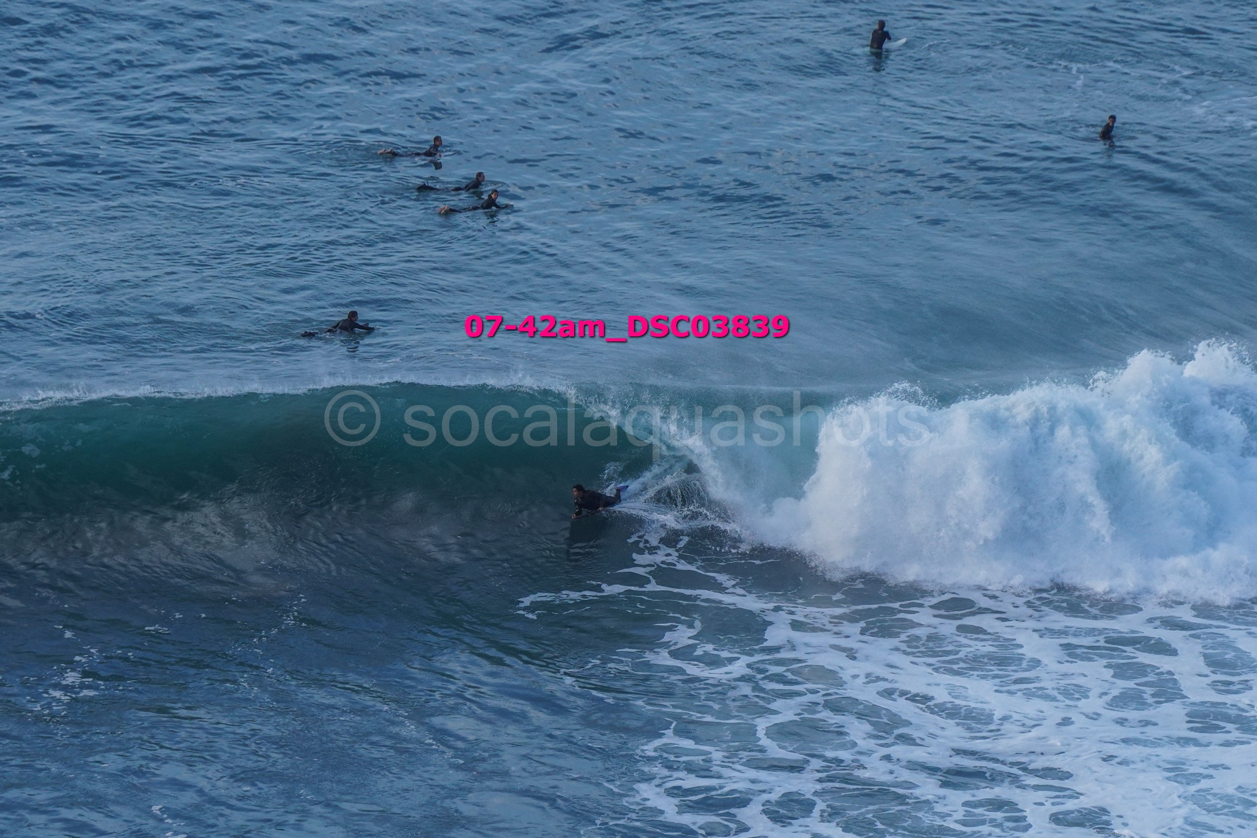 Surfer riding a wave while several people swim in the ocean in the background.
