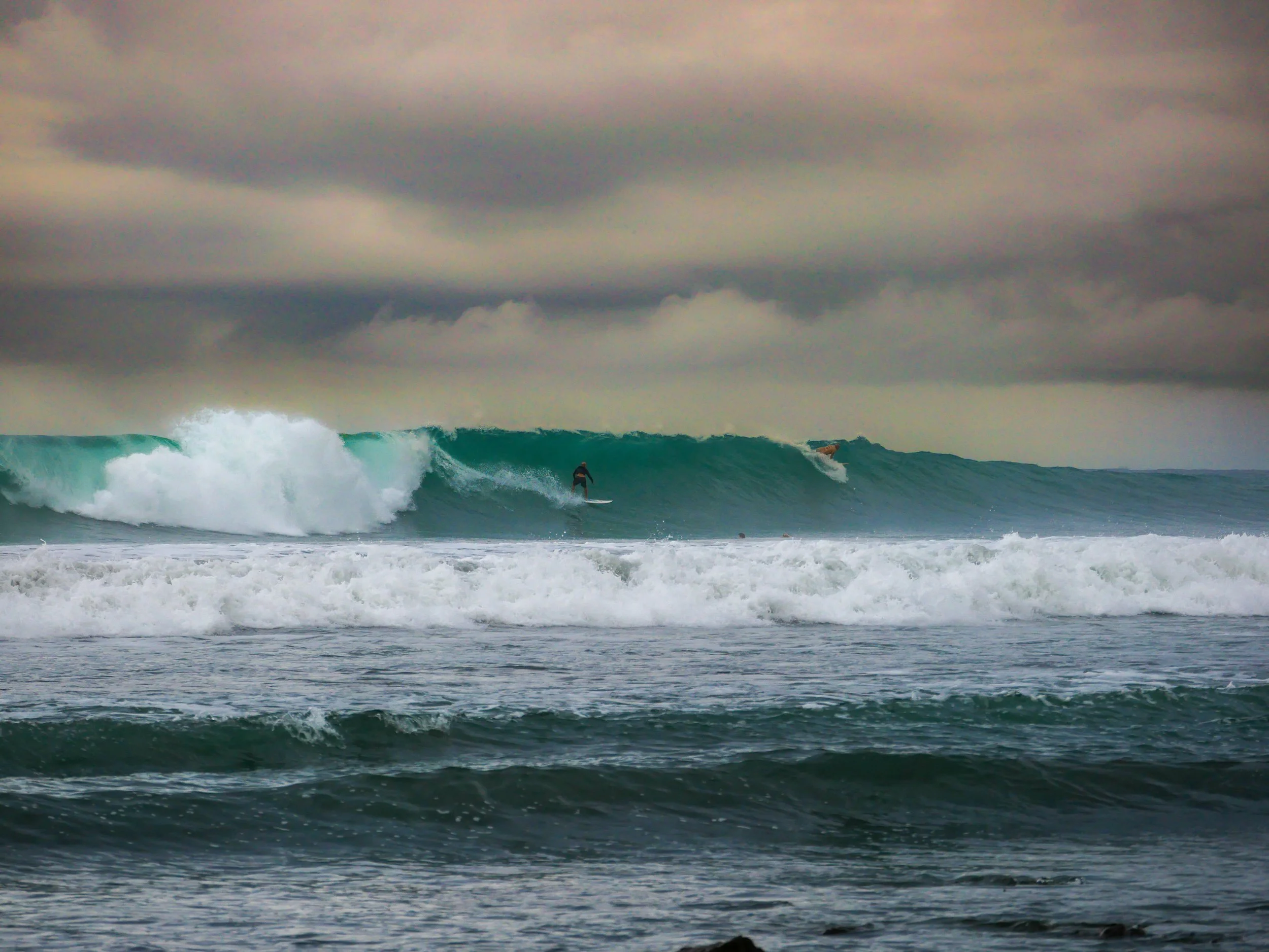 Surfer riding a large wave under cloudy sky at sea