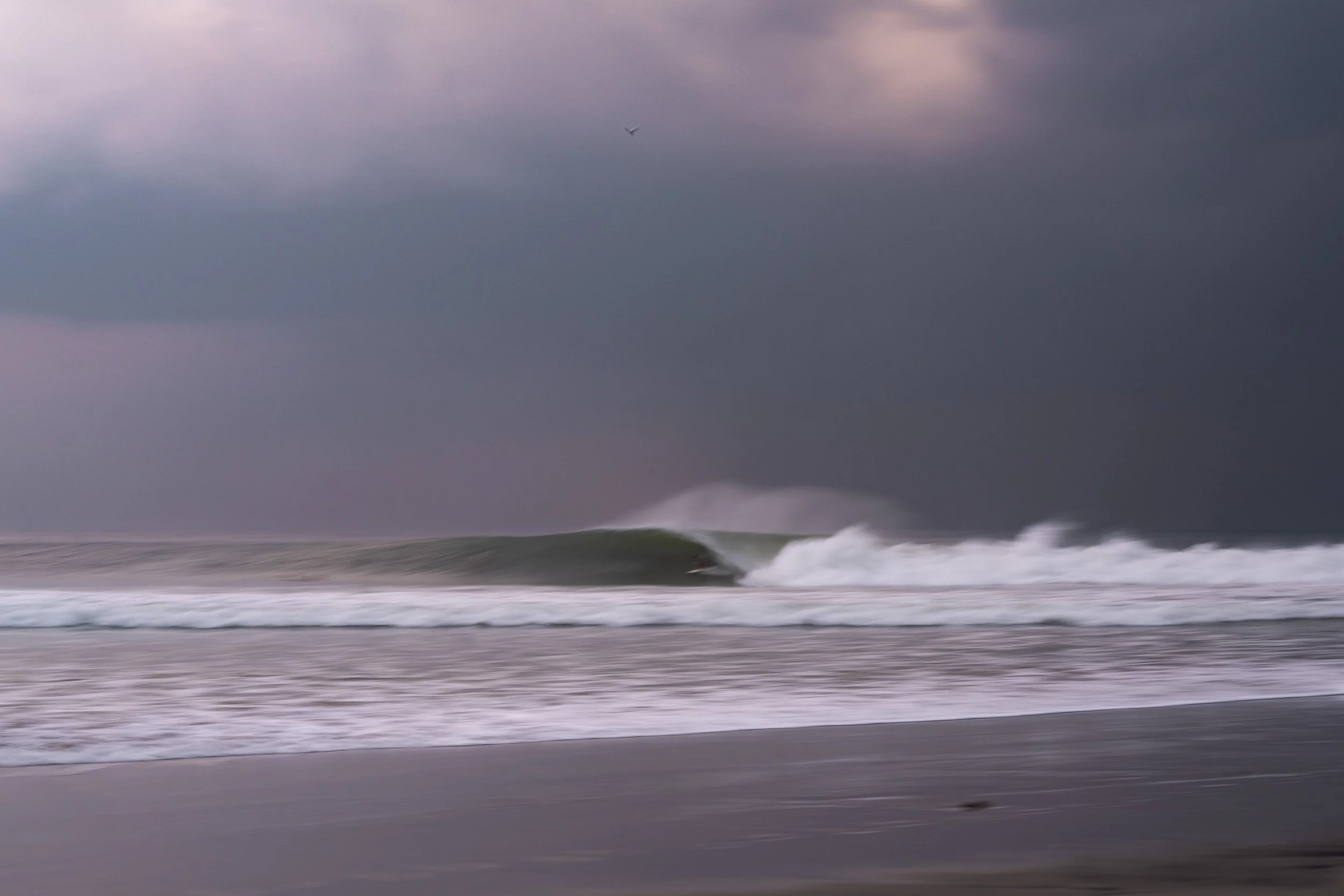 Dark stormy sky over a turbulent ocean with rolling waves approaching the shoreline.