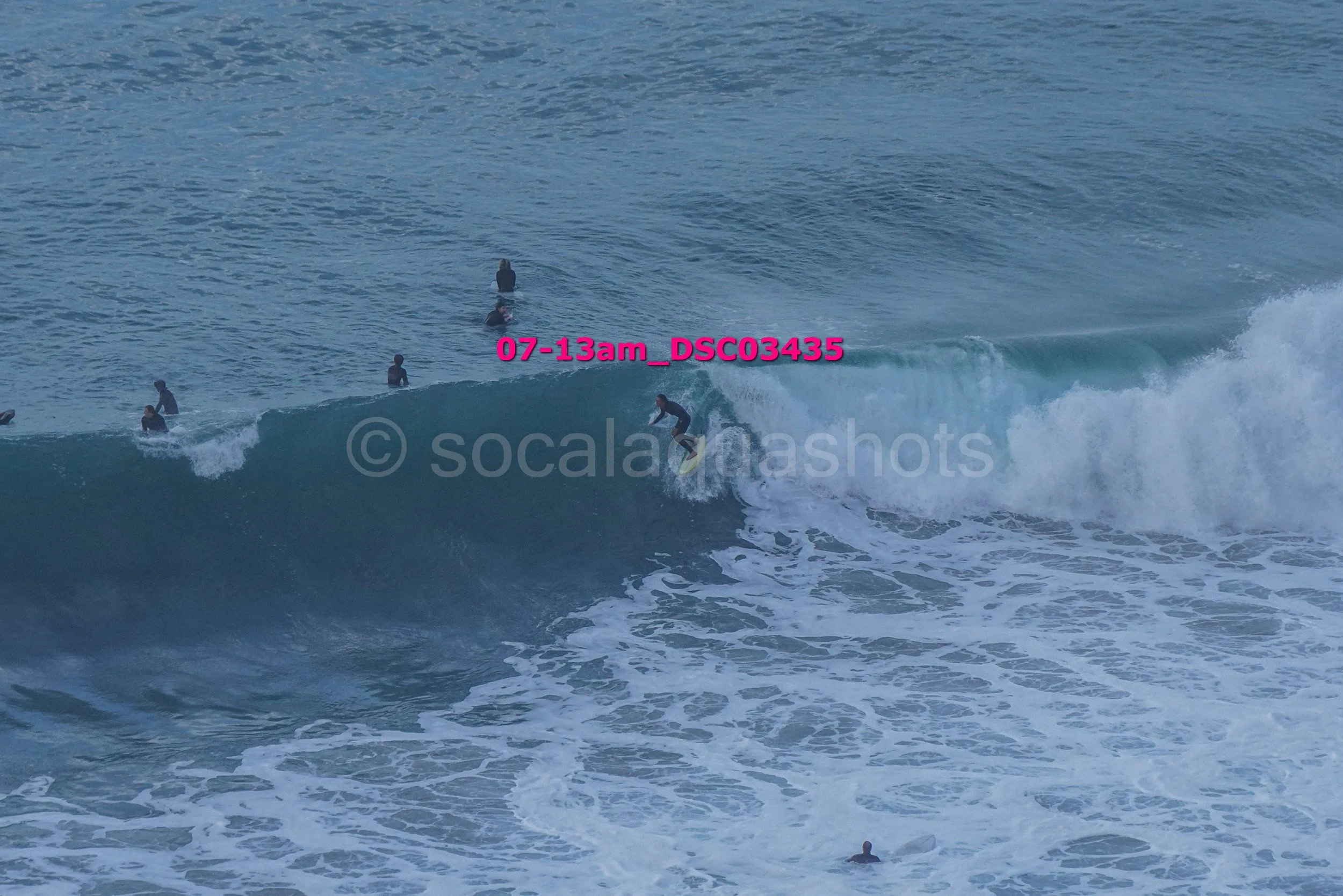 A person surfing on a wave with several people in the water watching