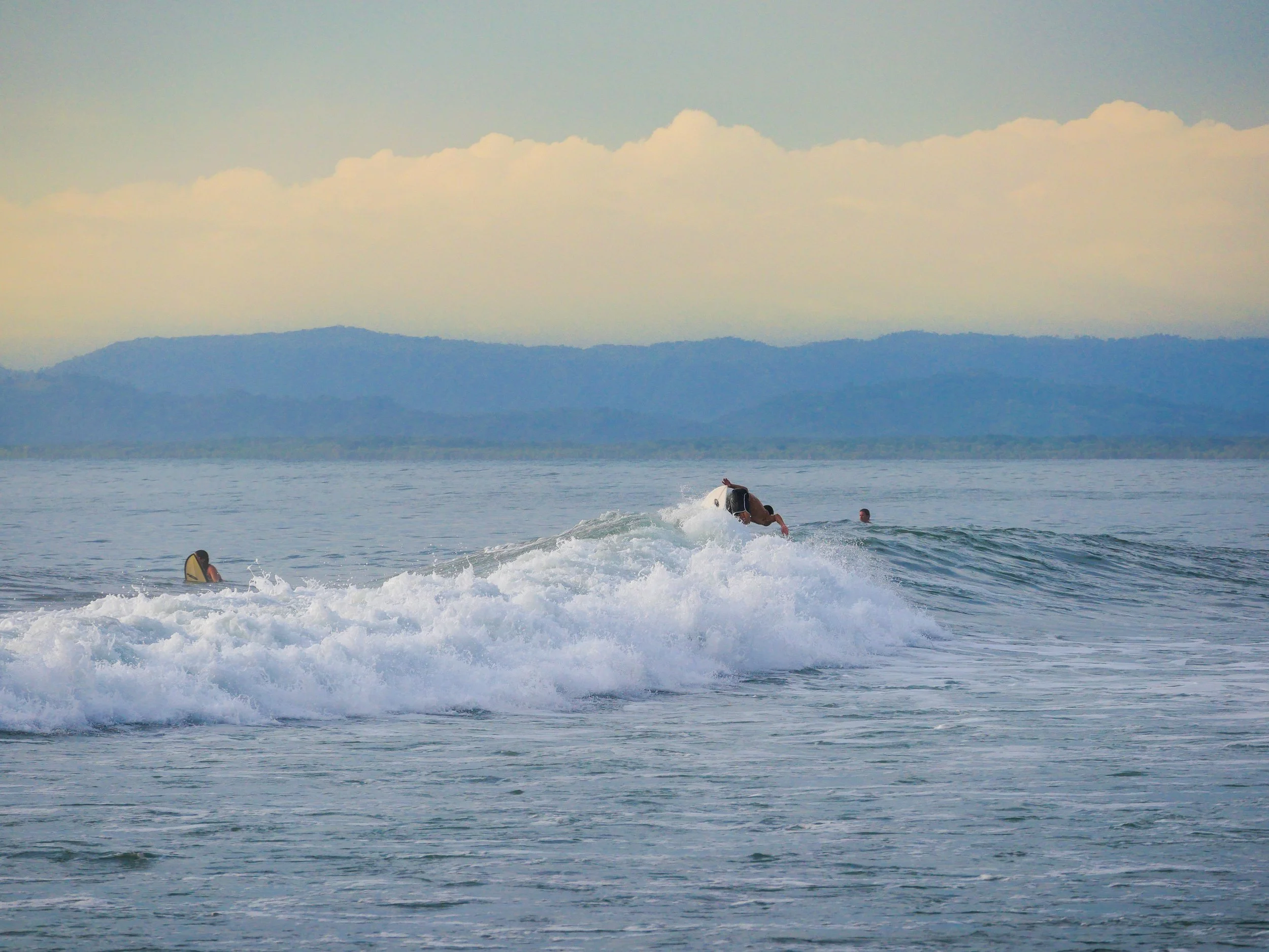 Surfers paddling in ocean waves with mountains and cloudy sky in background