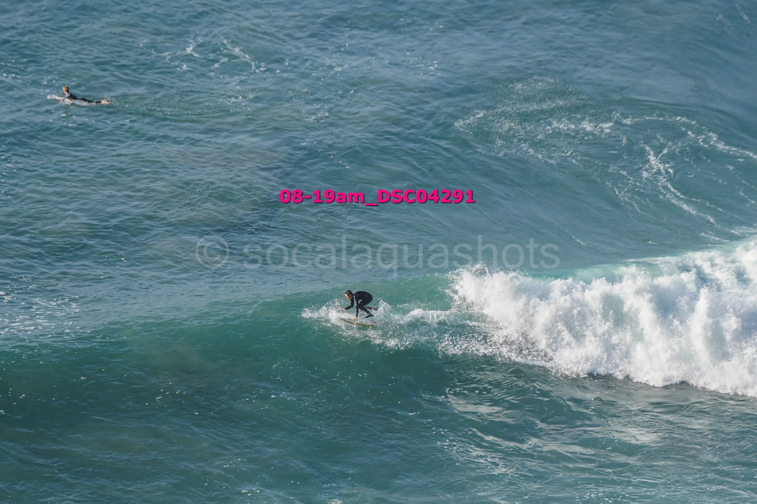 Surfer riding a wave in the ocean with another person swimming in the distance.