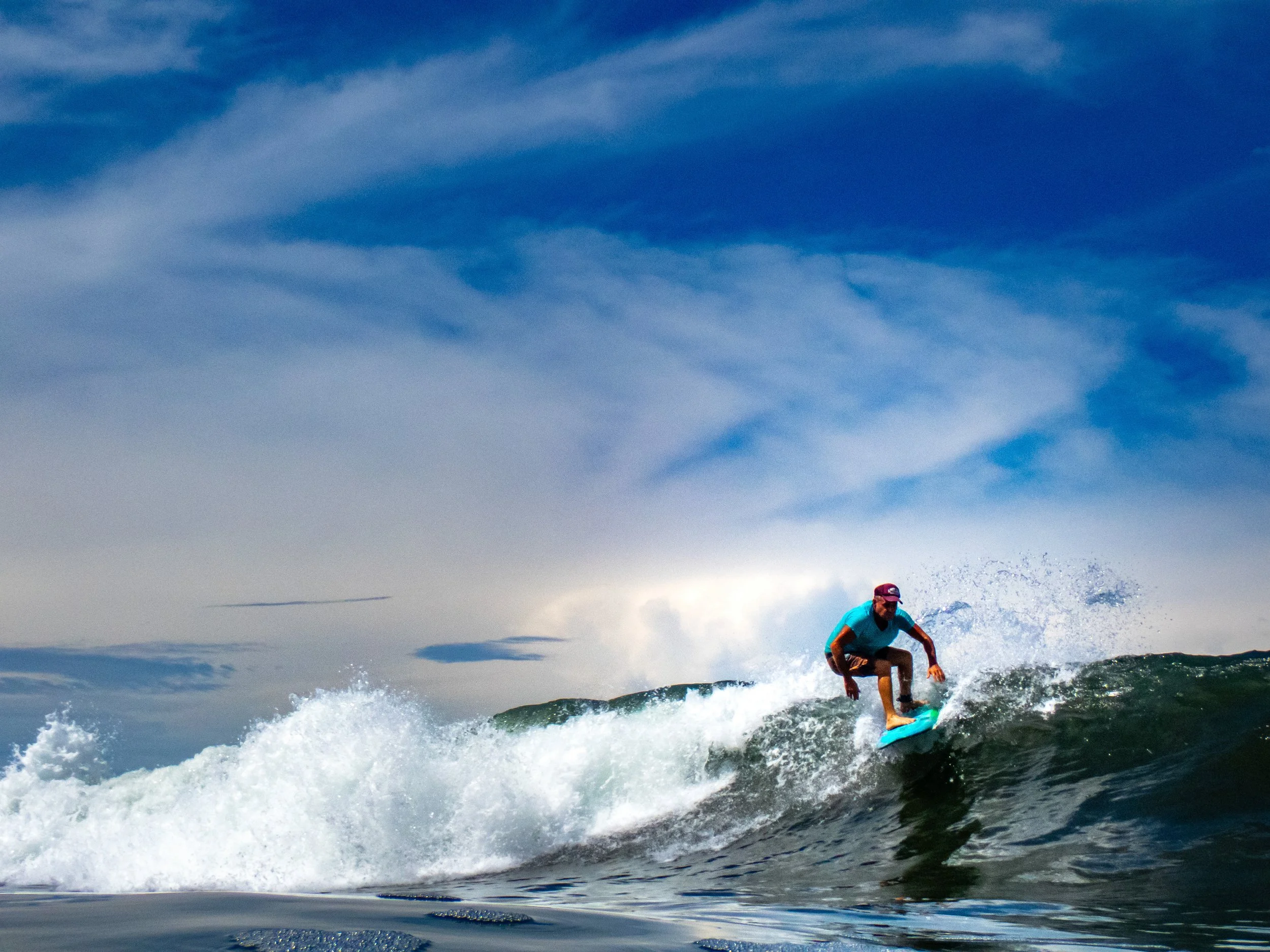 A person surfing on a wave in the ocean under a partly cloudy sky.