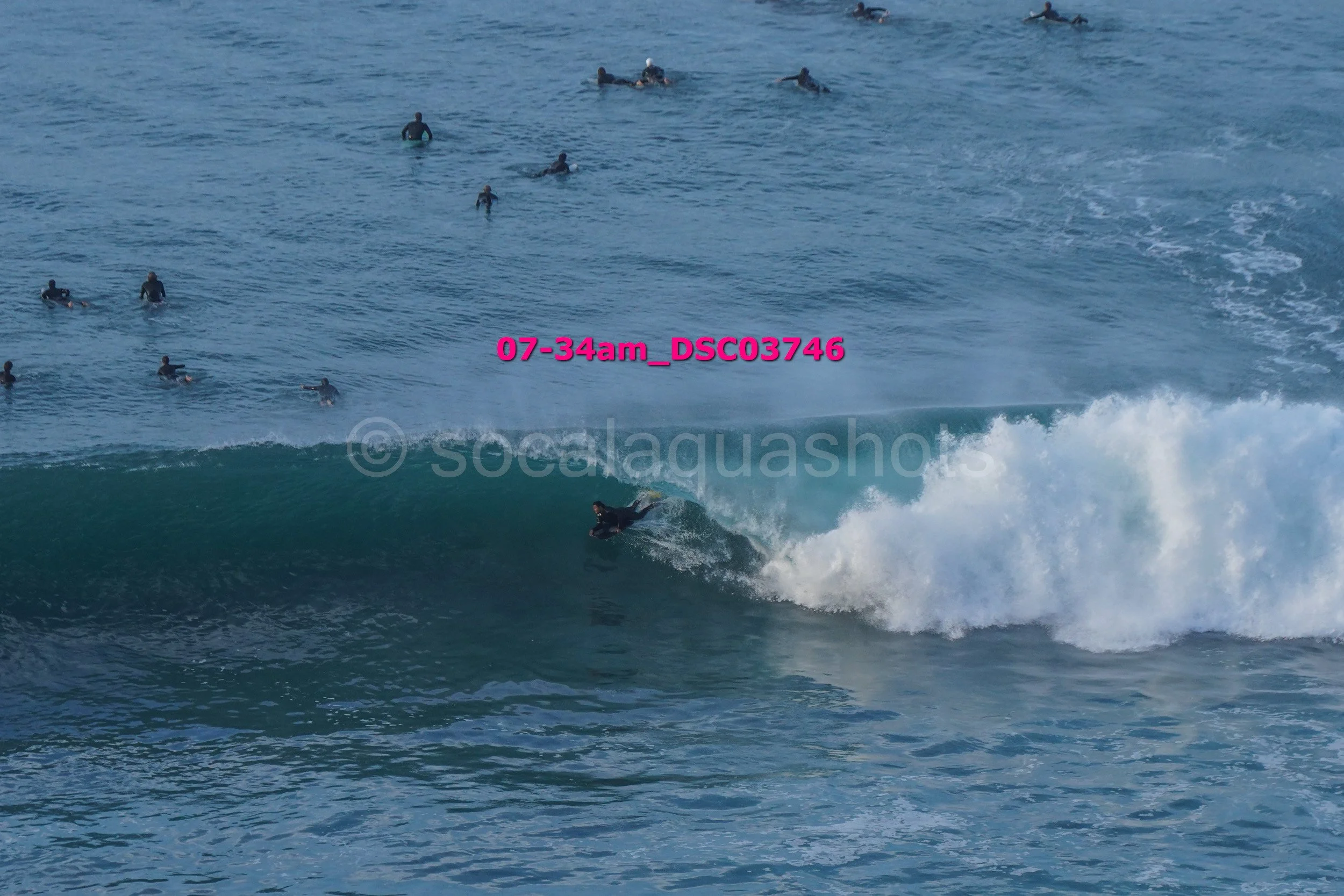 Surfer riding a wave while a group of surfers wait in the water behind.