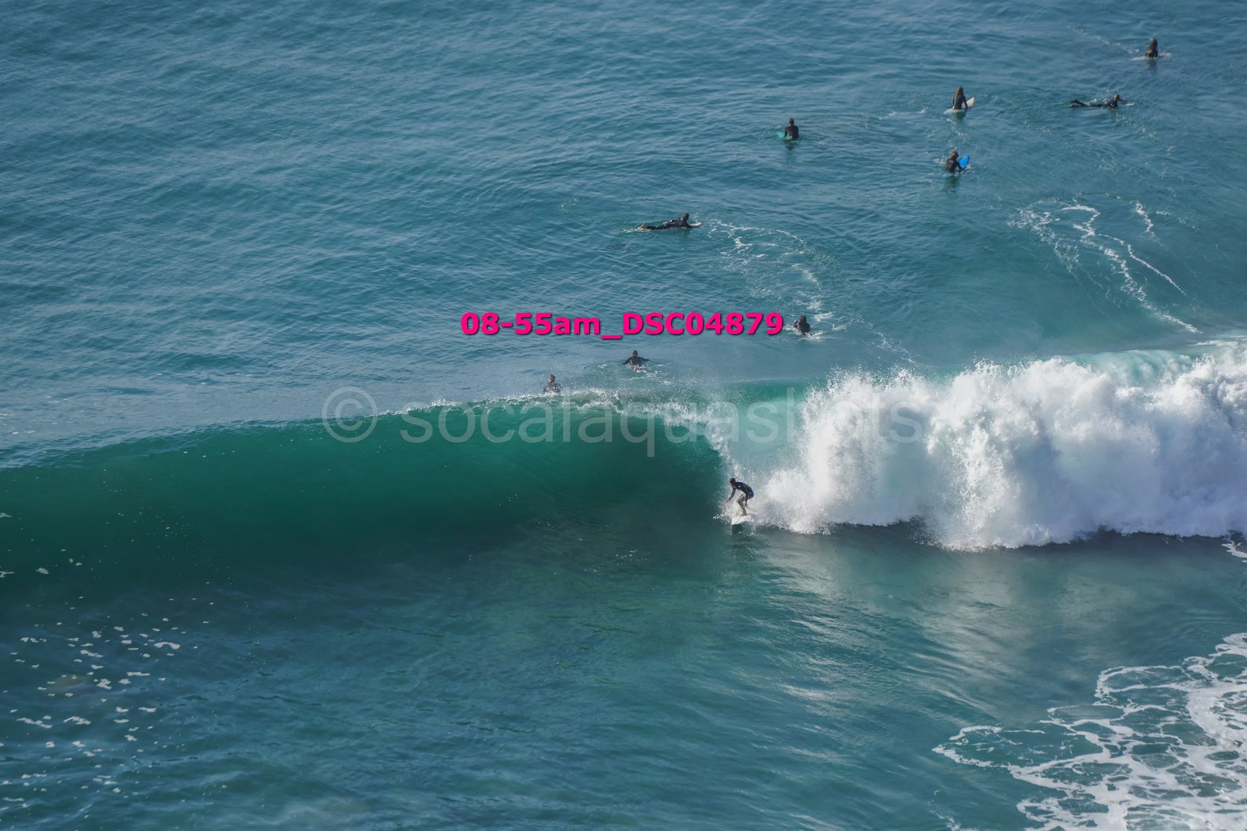 A surfer riding a large wave with multiple people in the water watching from behind.