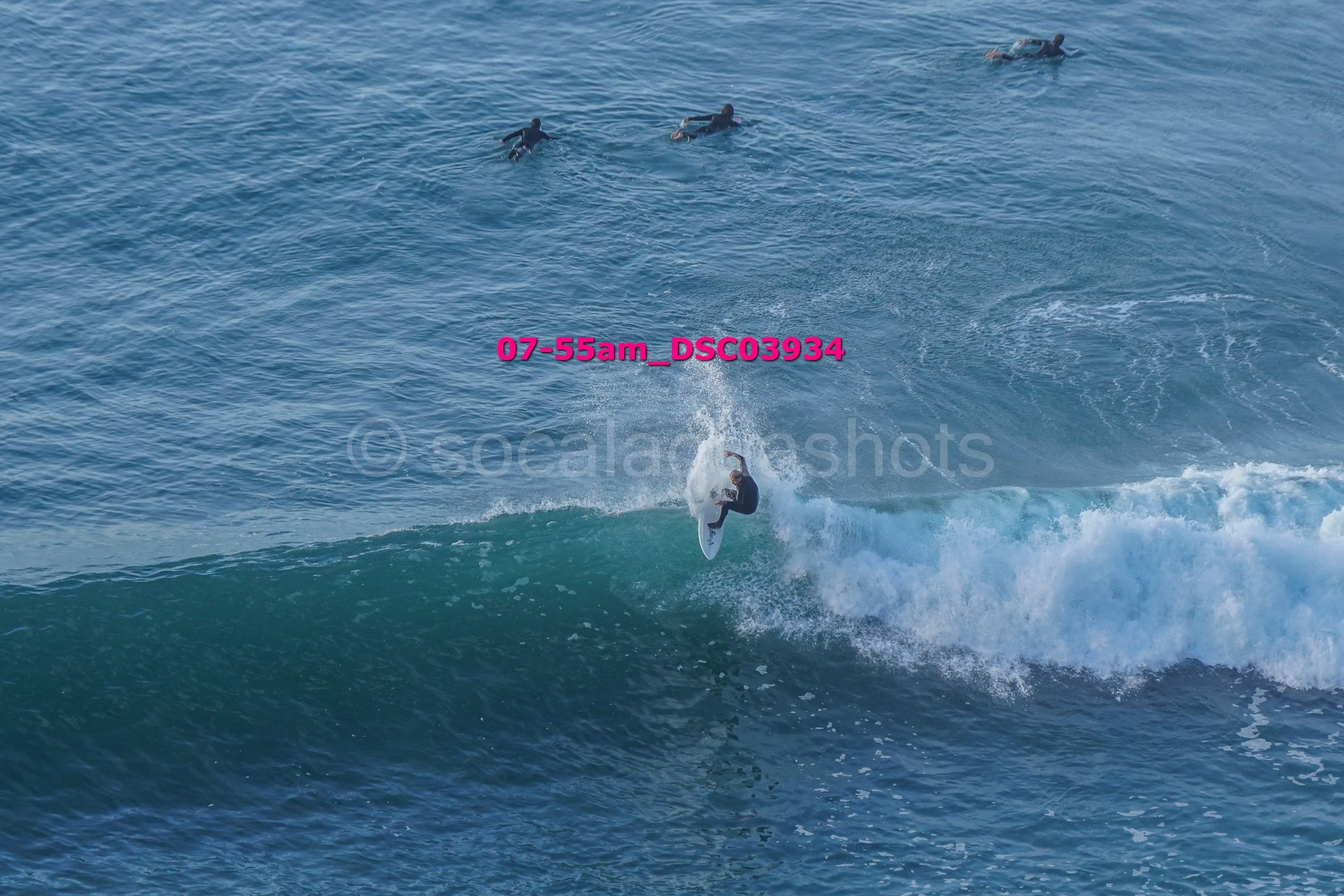 Surfer performing a maneuver on a wave while four other surfers are paddling in the water.
