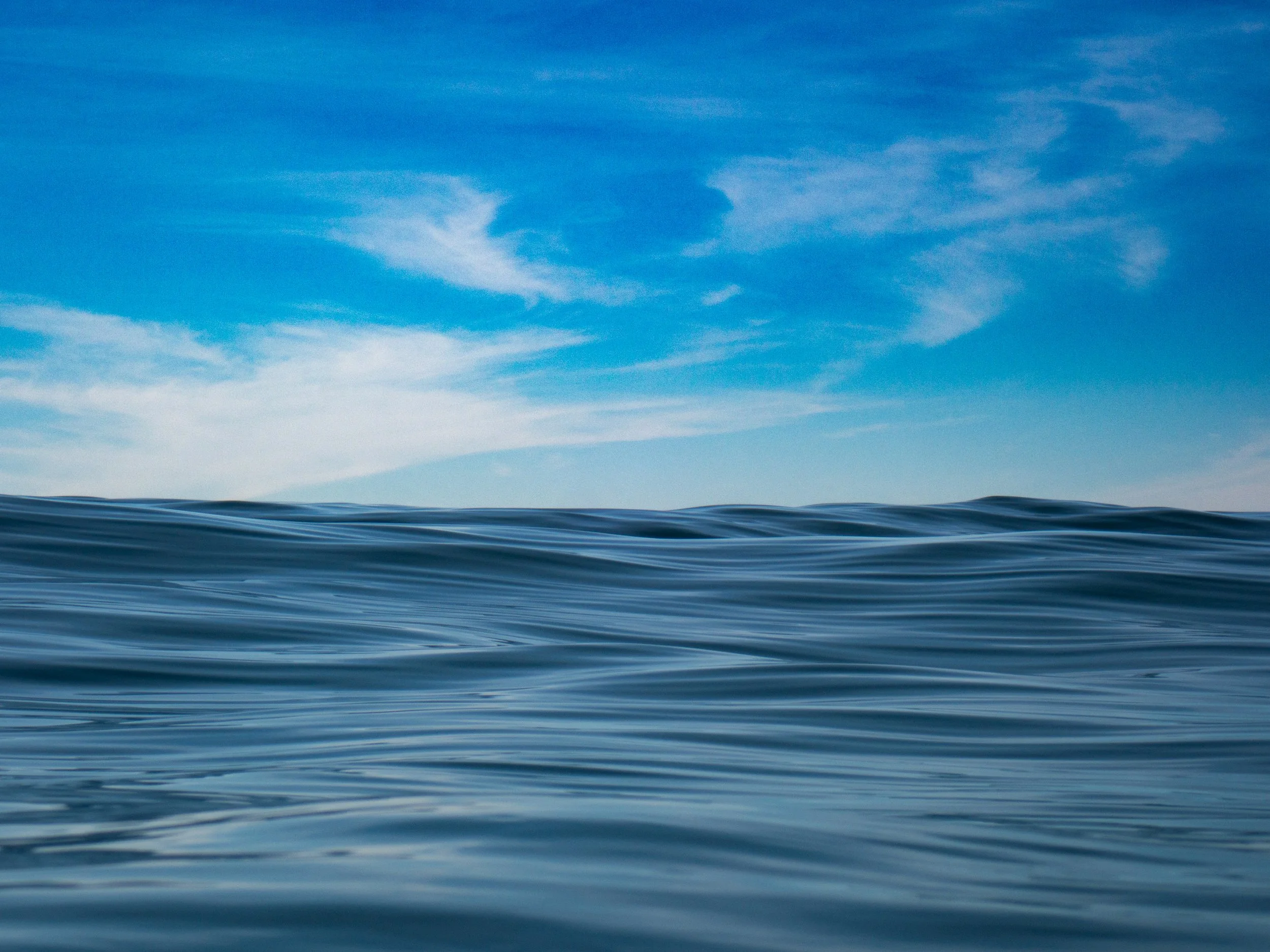 Calm ocean surface with gentle waves under a partly cloudy blue sky