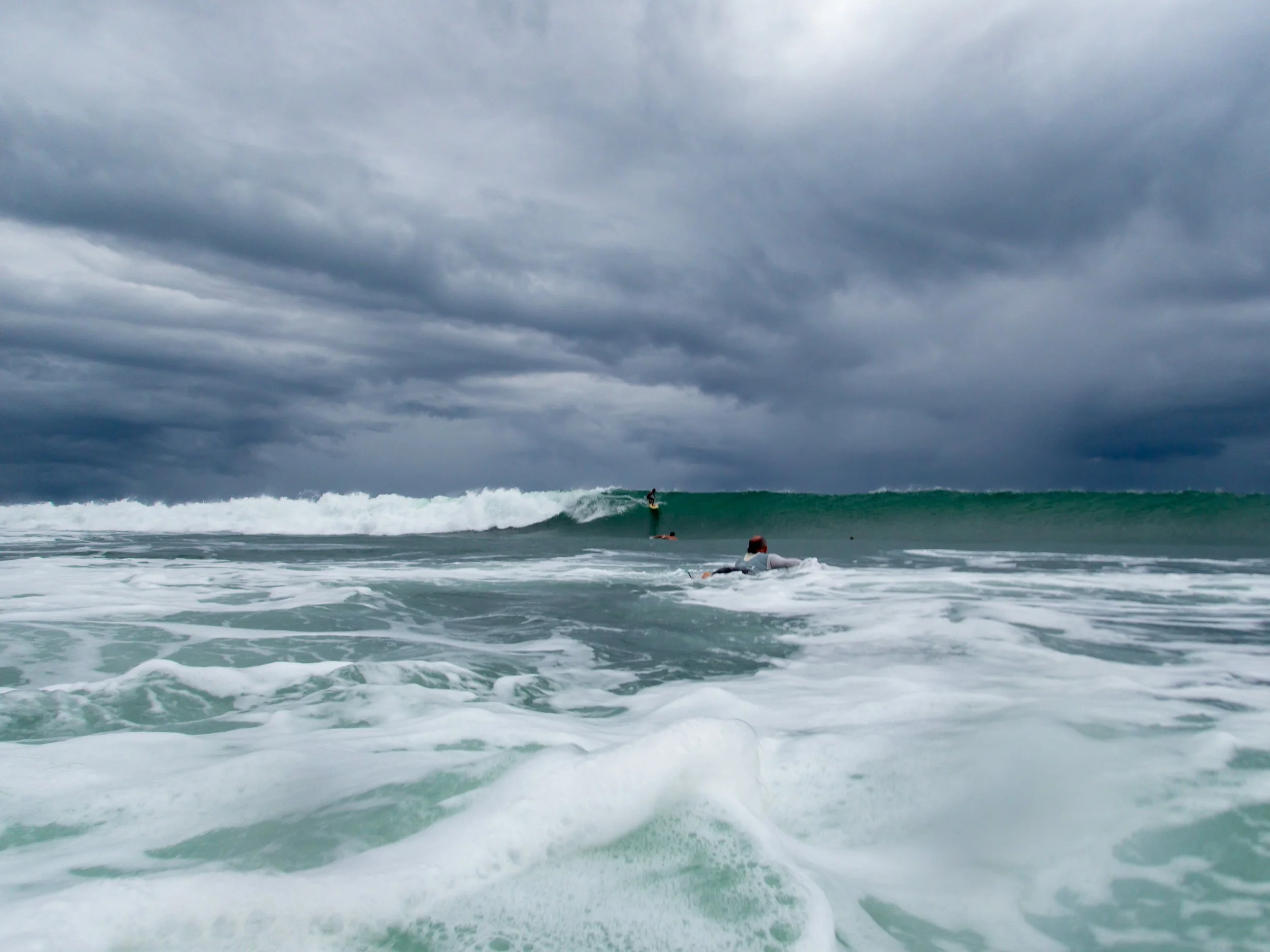 Surfer paddling in ocean with large waves under cloudy sky