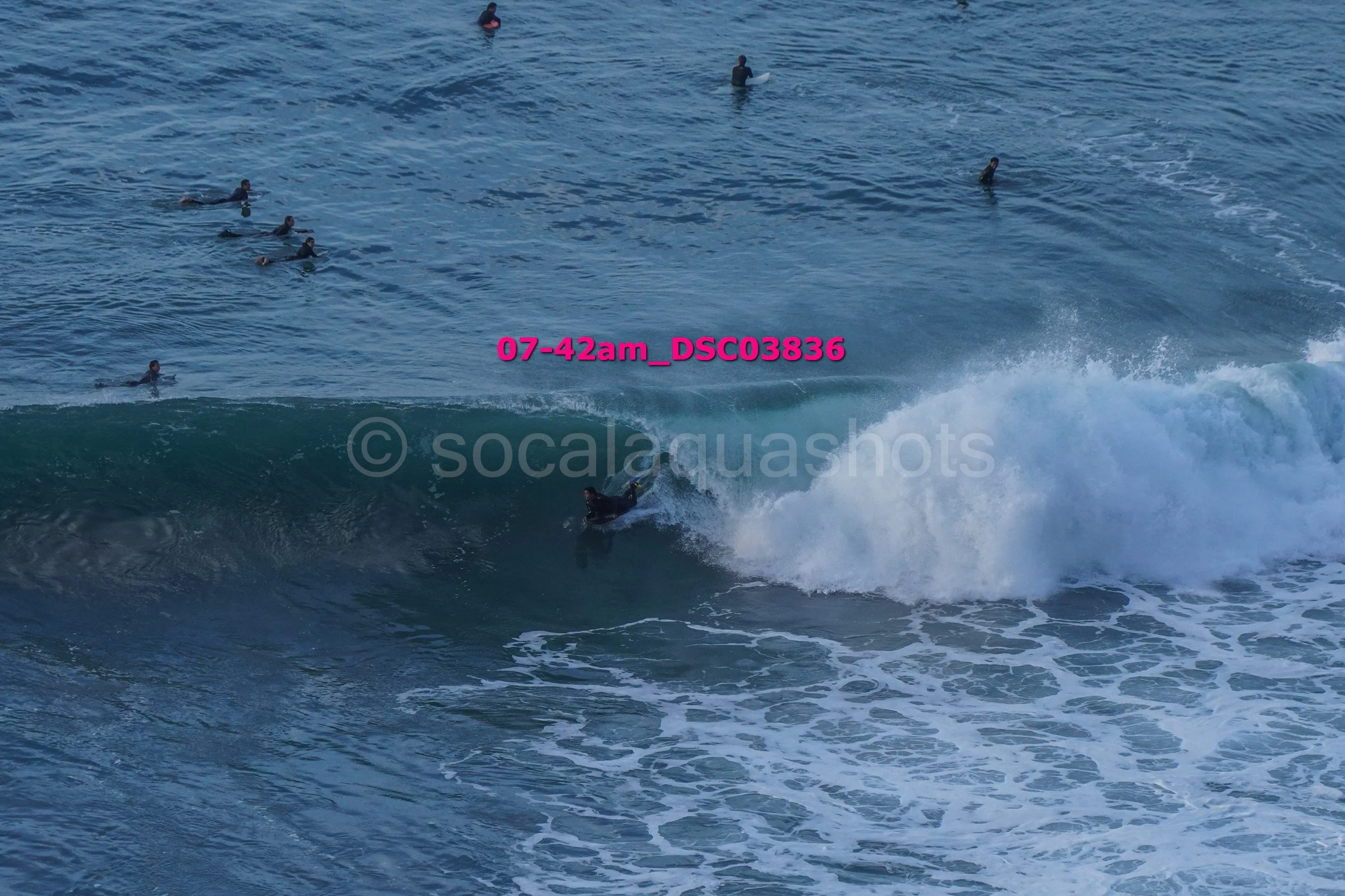 Surfer riding a wave with multiple surfers in the water nearby.