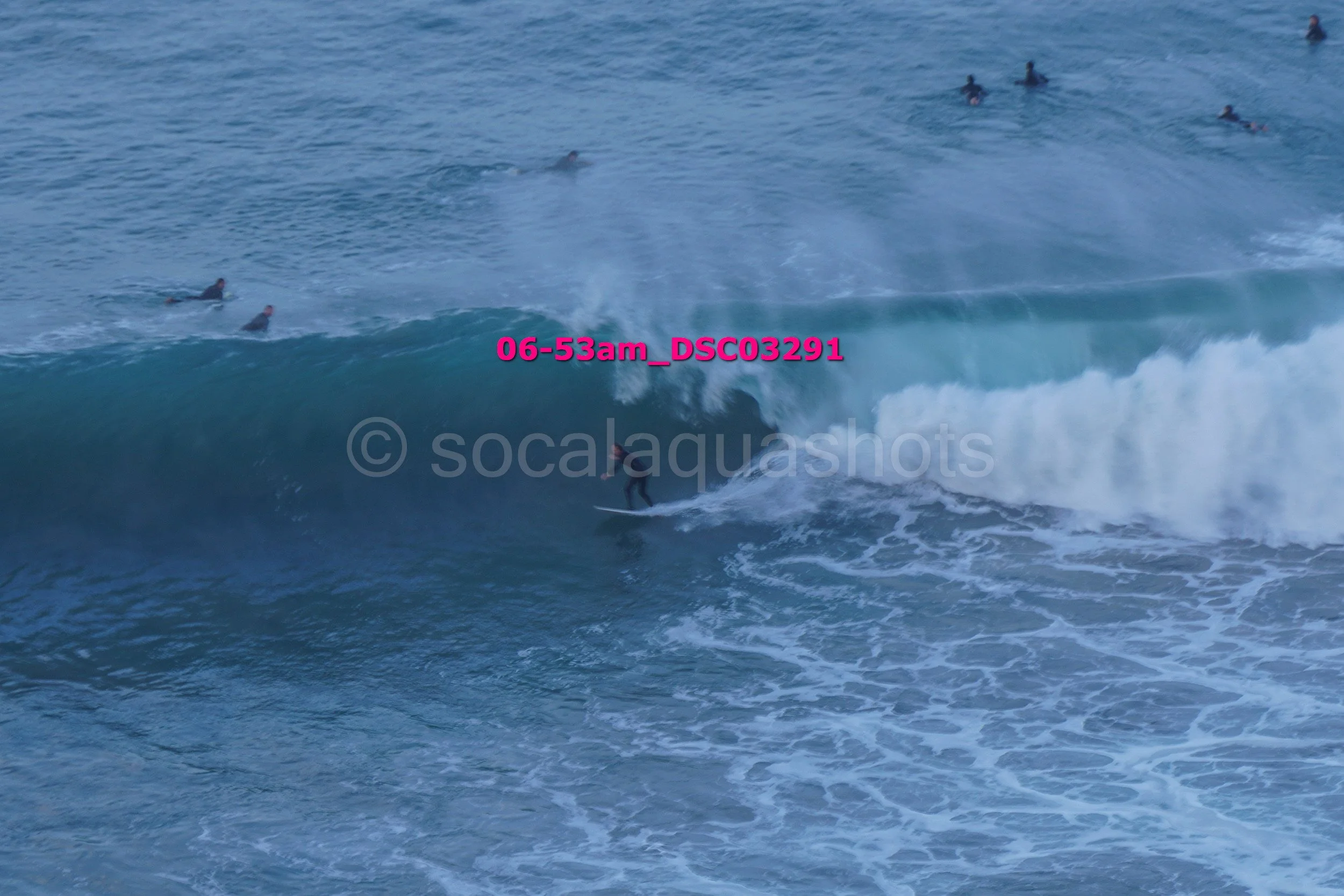 Surfer riding a wave with multiple swimmers in the background at the beach.