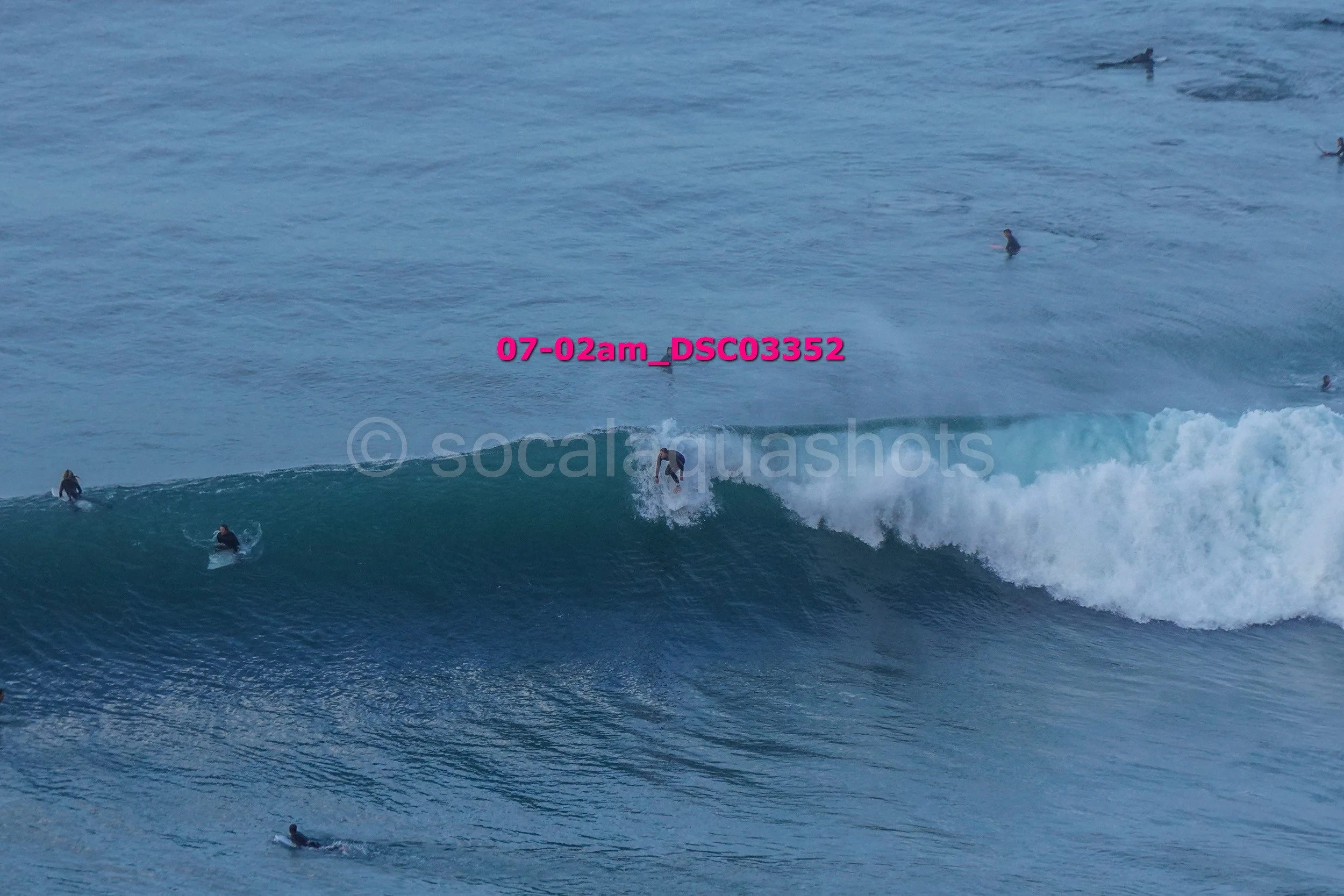 A group of surfers in the ocean, with one surfer riding a wave while others wait or paddle in the water.