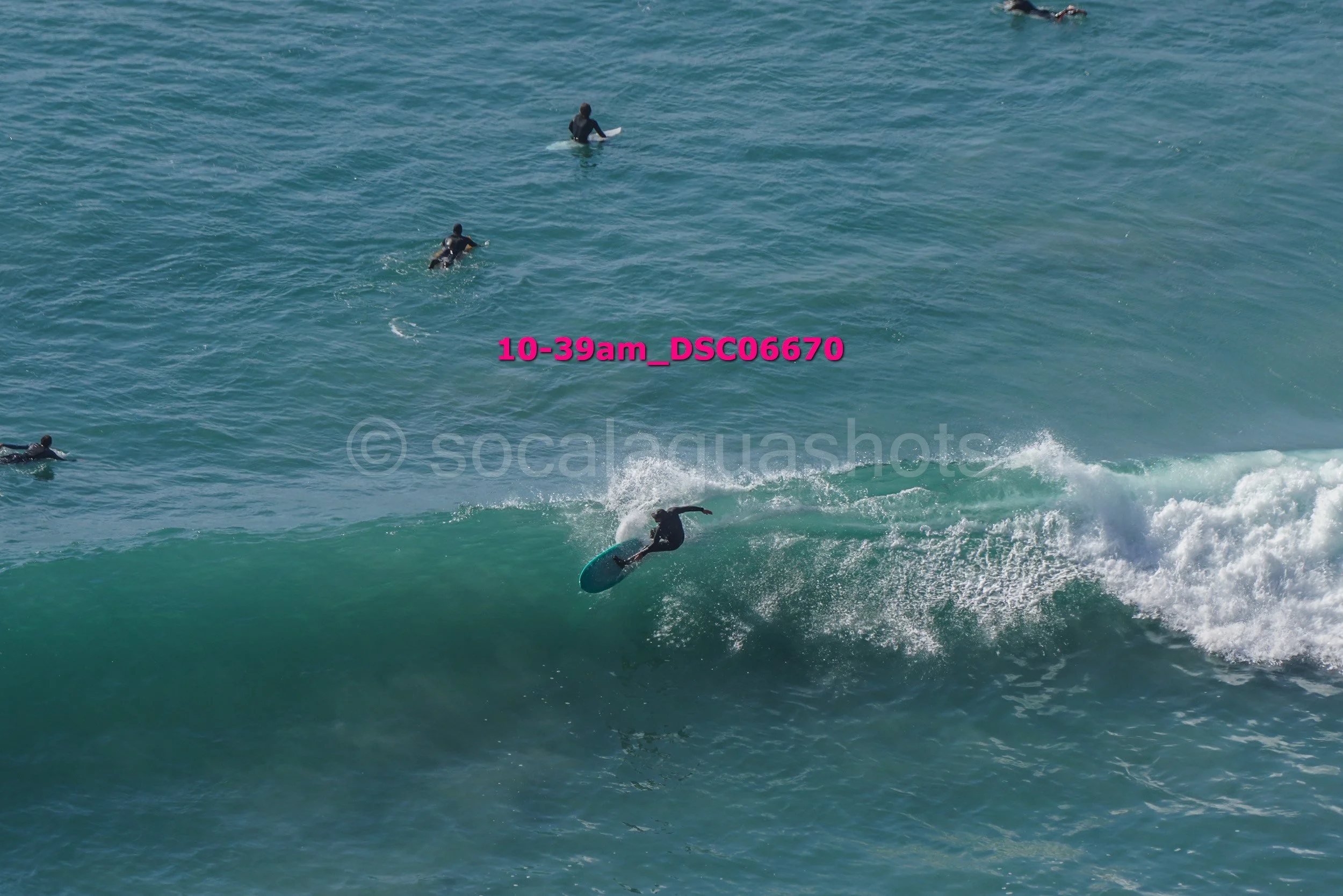 Surfer riding a wave with four surfers in the background in open water.