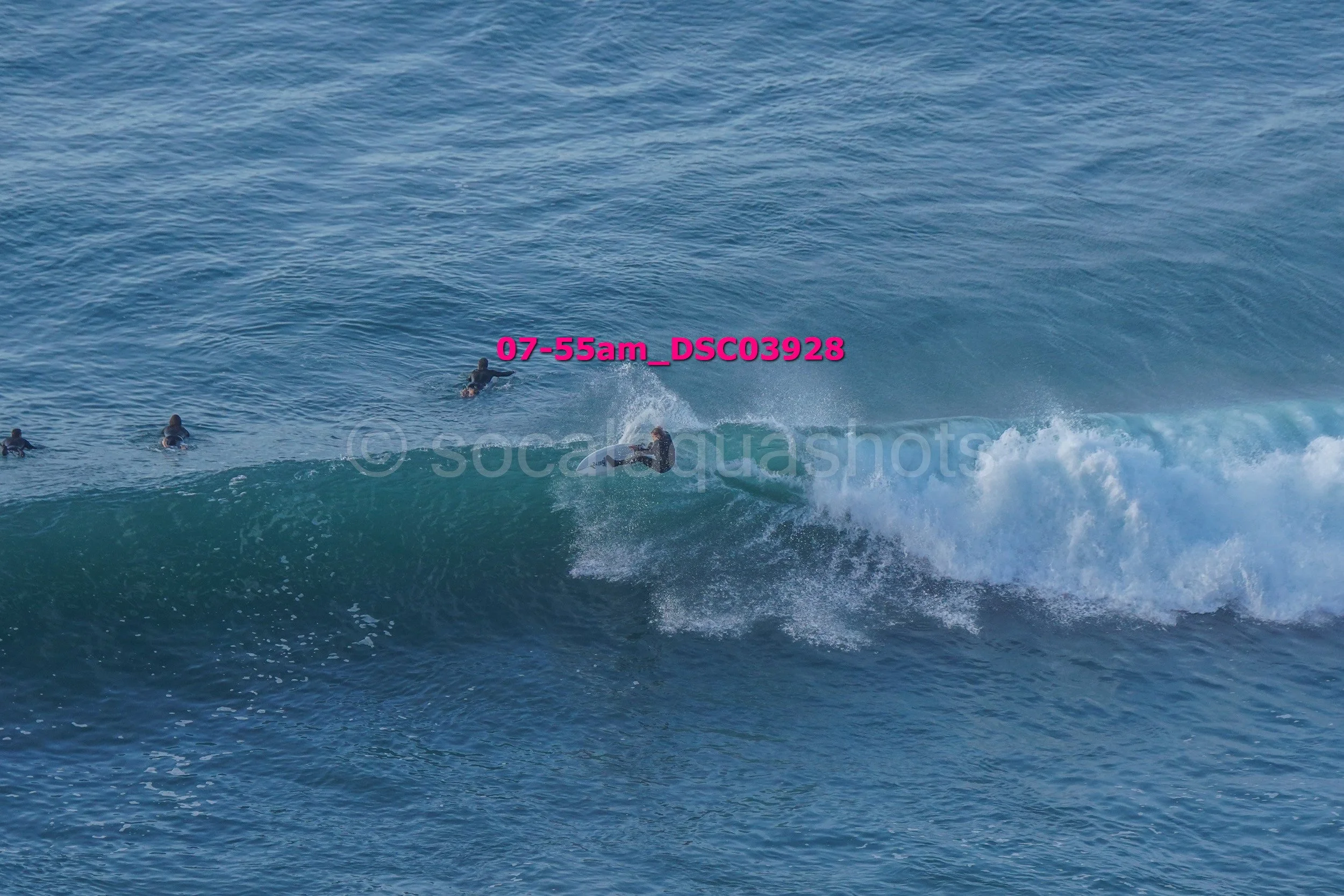 Surfer riding a wave in the ocean with three other surfers nearby, who are waiting for their turn.