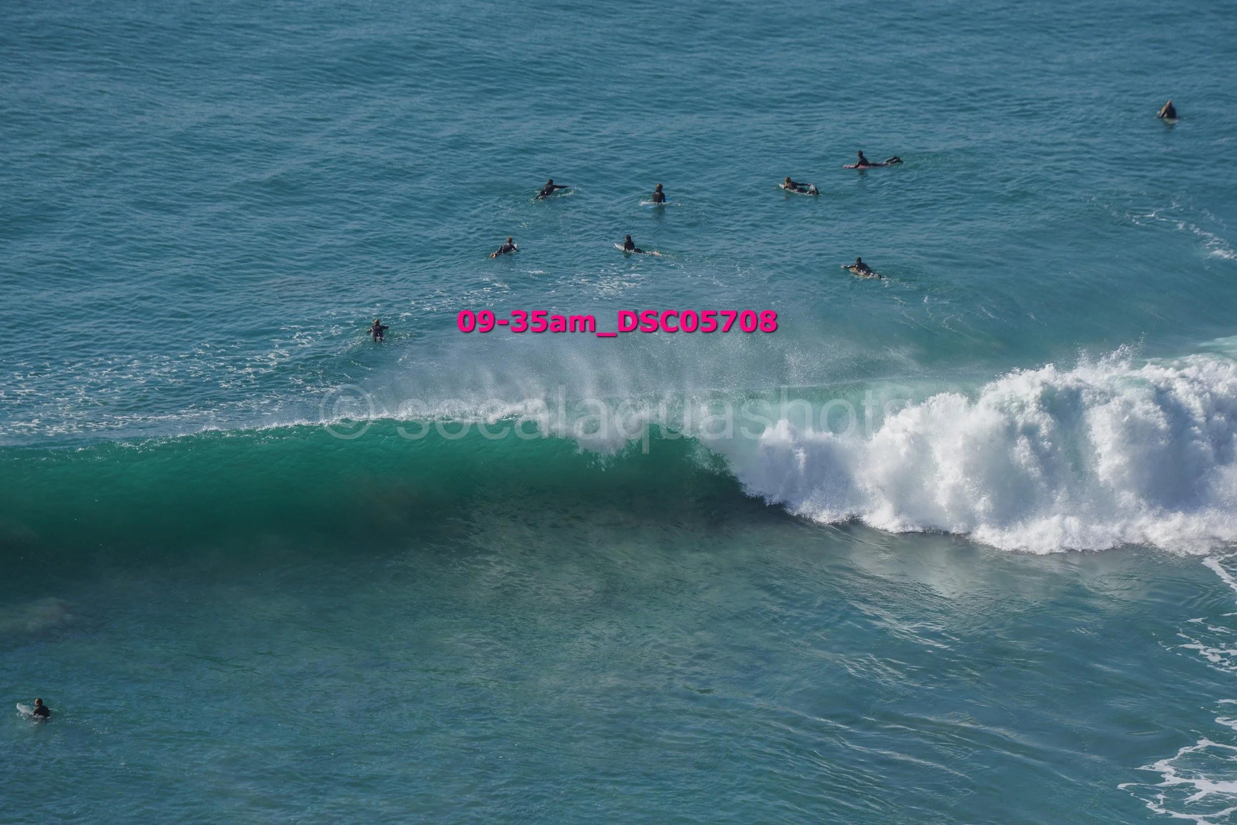 Surfers in the ocean waiting for waves with one large wave approaching.