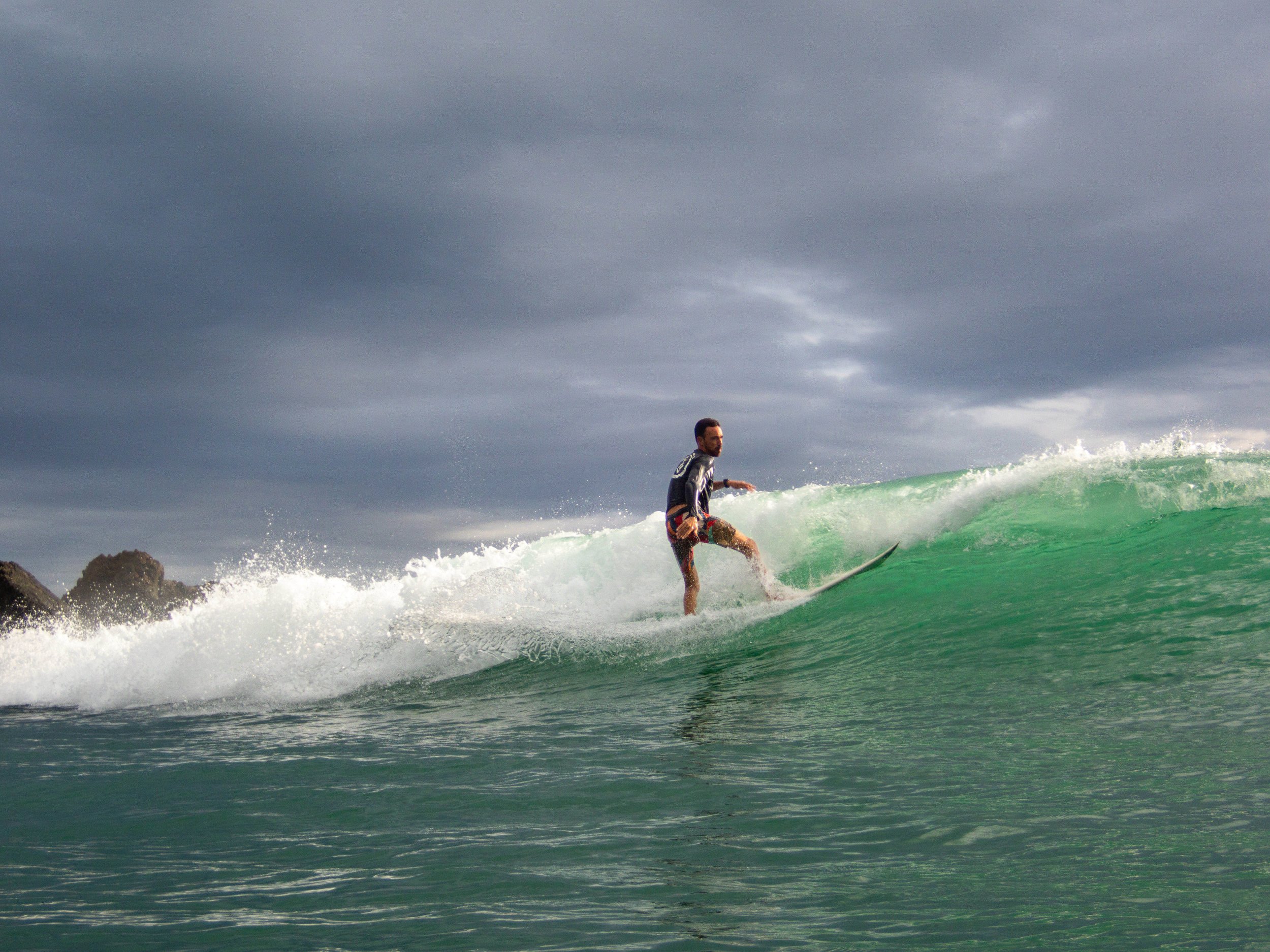 Surfer riding a wave in the ocean under a cloudy sky.