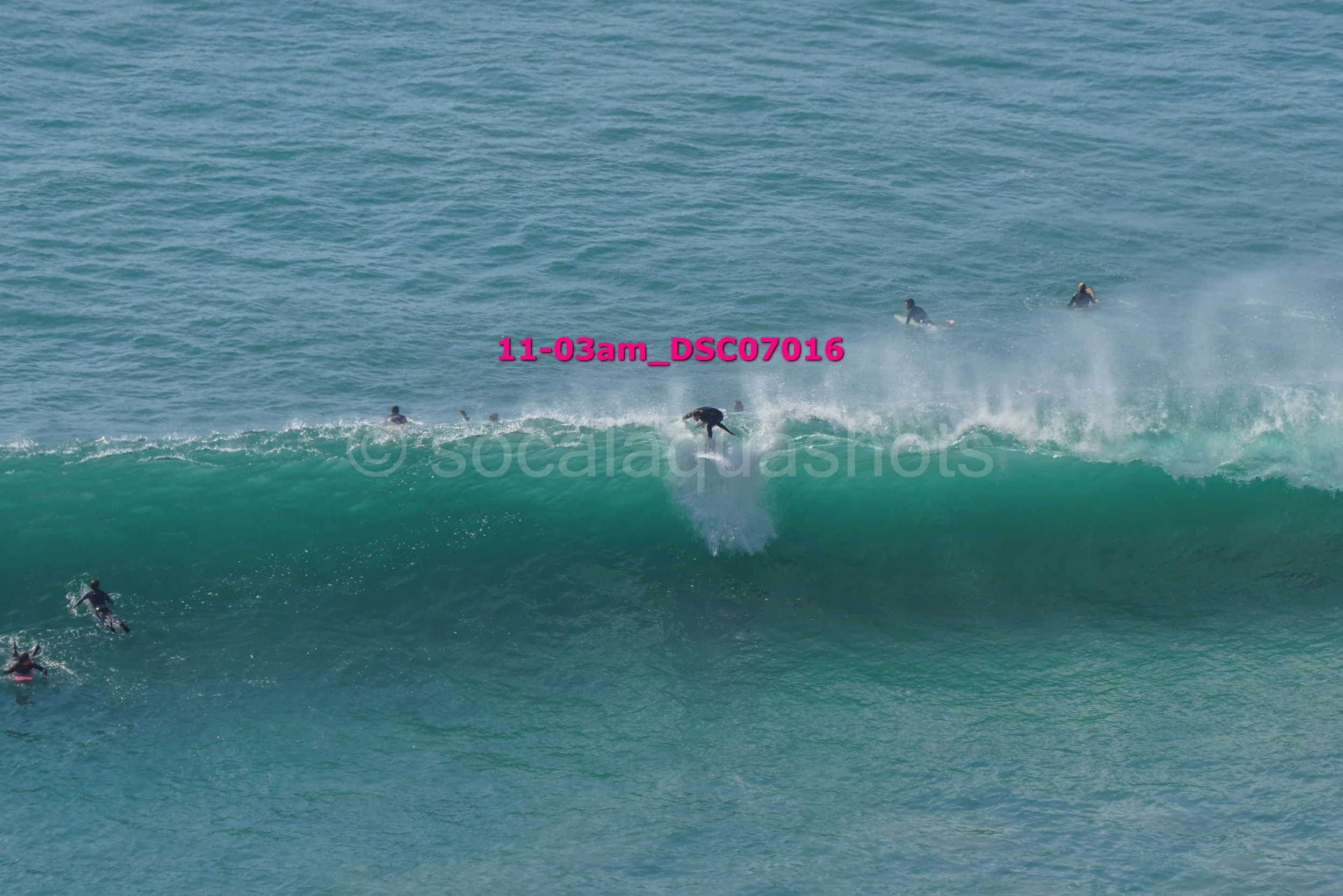 Surfer riding a large wave with several people in the water watching from the background.