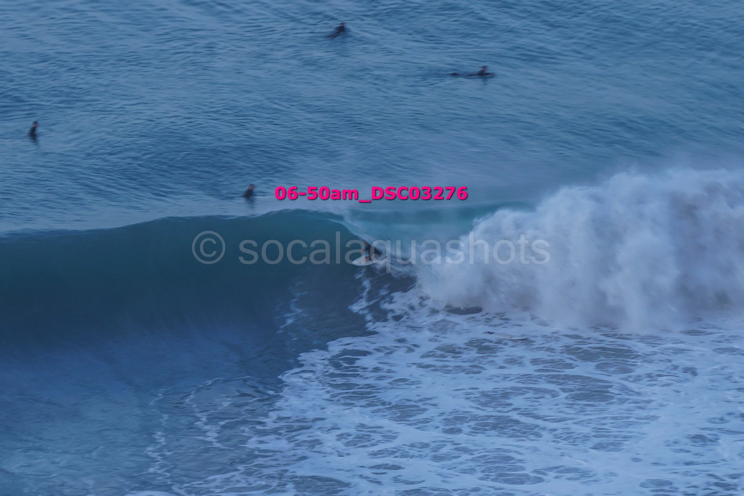 A surfer riding a wave with several people in the water watching from a distance, ocean scene during daylight.