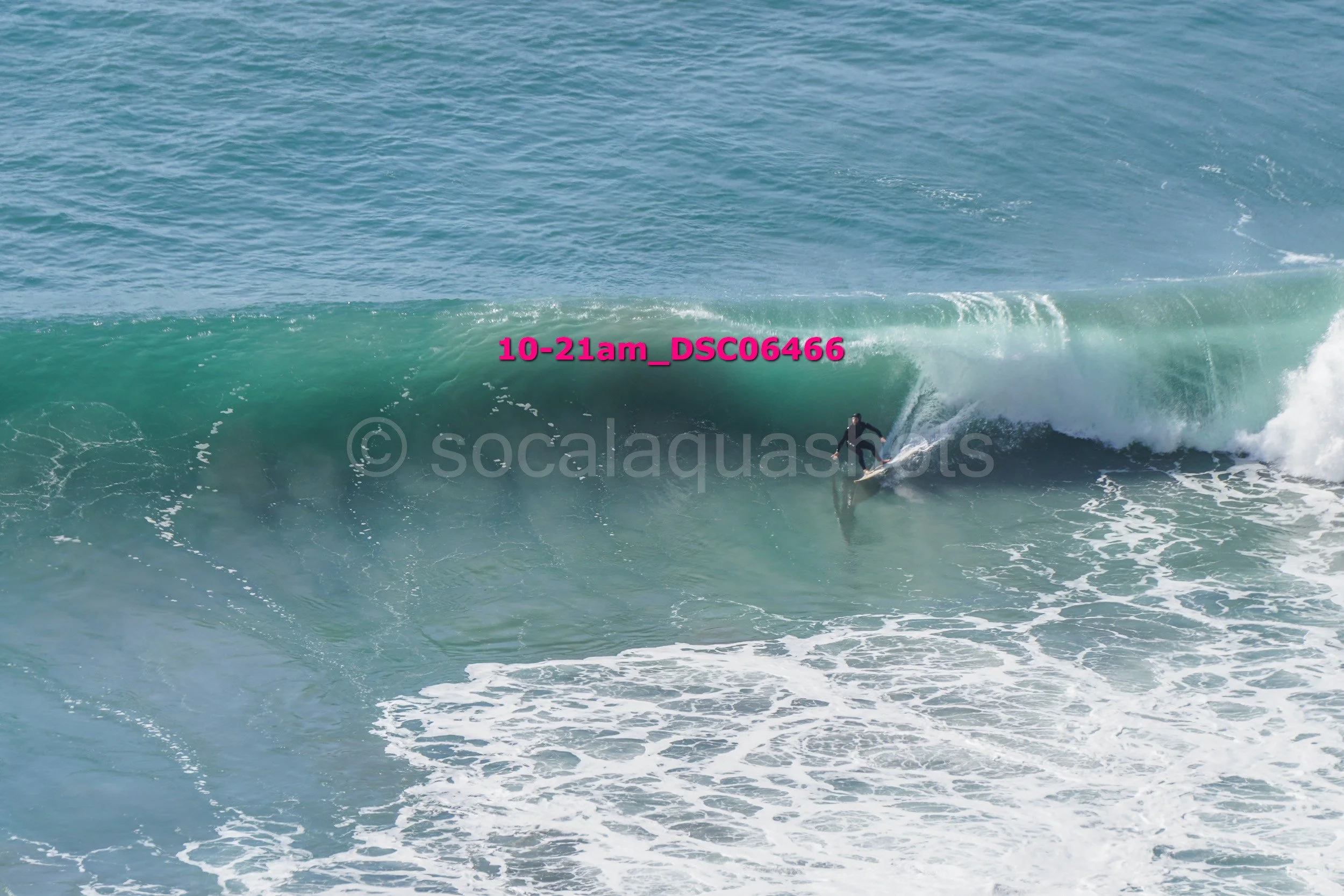 A surfer riding inside a large ocean wave with white foam at the shore.