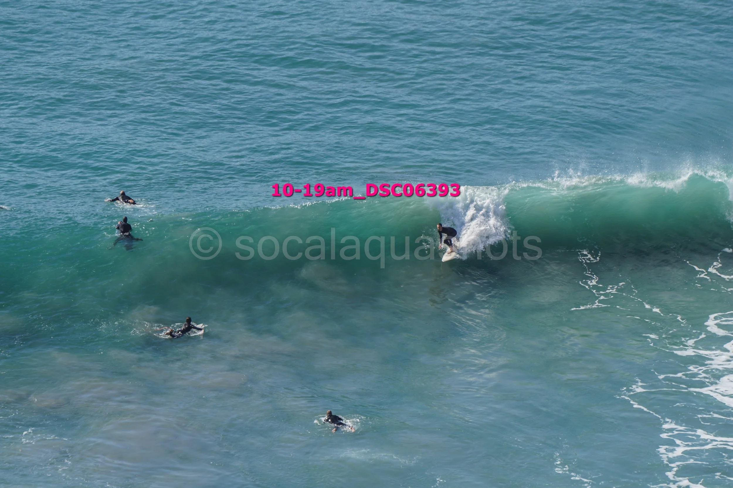 A person surfing on a wave while several others are paddling on surfboards in the water.