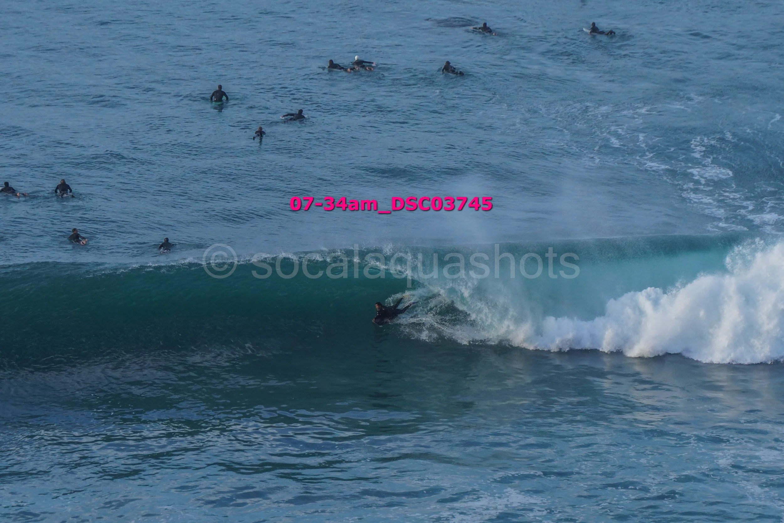 A group of surfers in wetsuits riding and waiting on waves in the ocean.