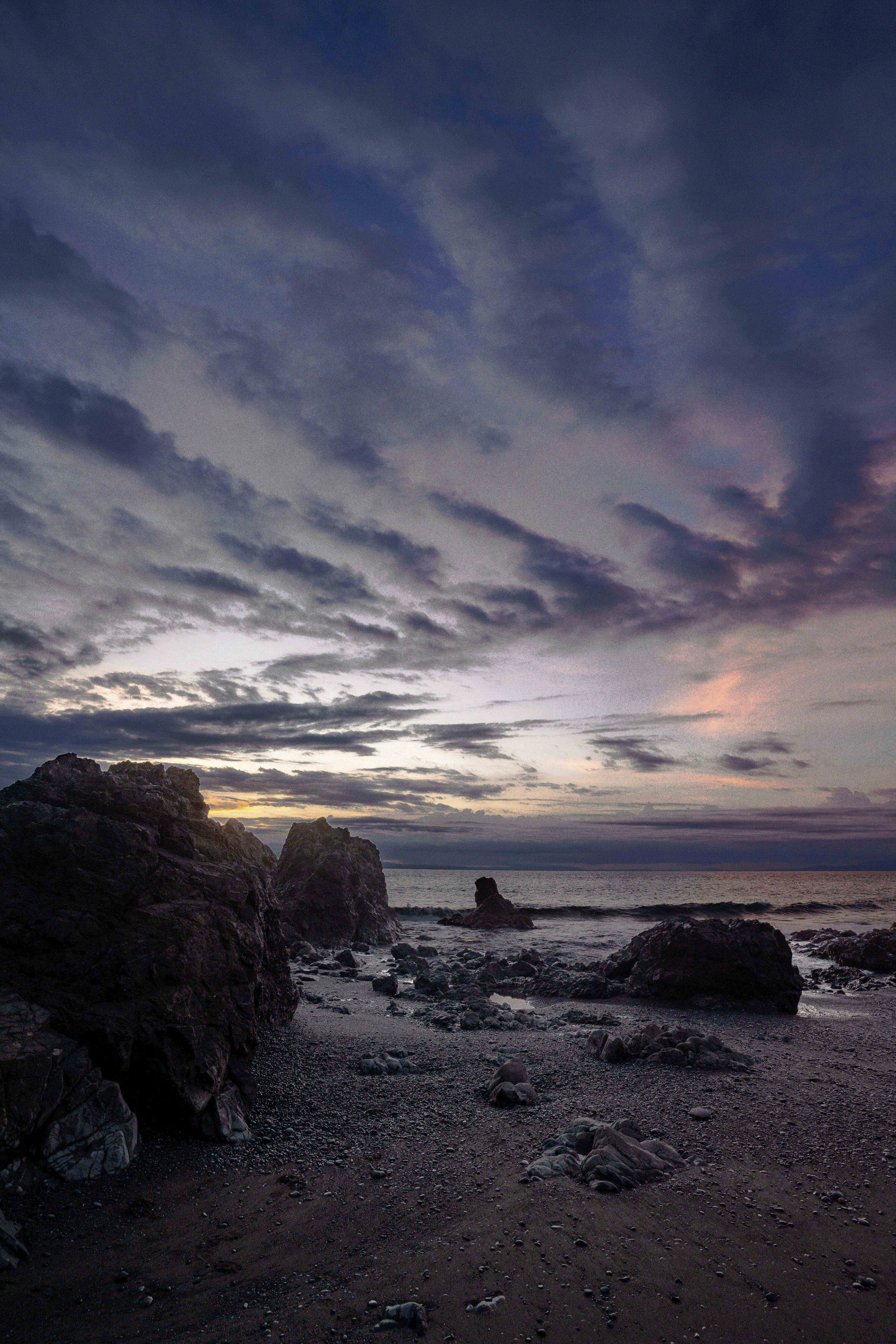 A beach at dusk with rocky shoreline, dark clouds in the sky, and the ocean in the background.