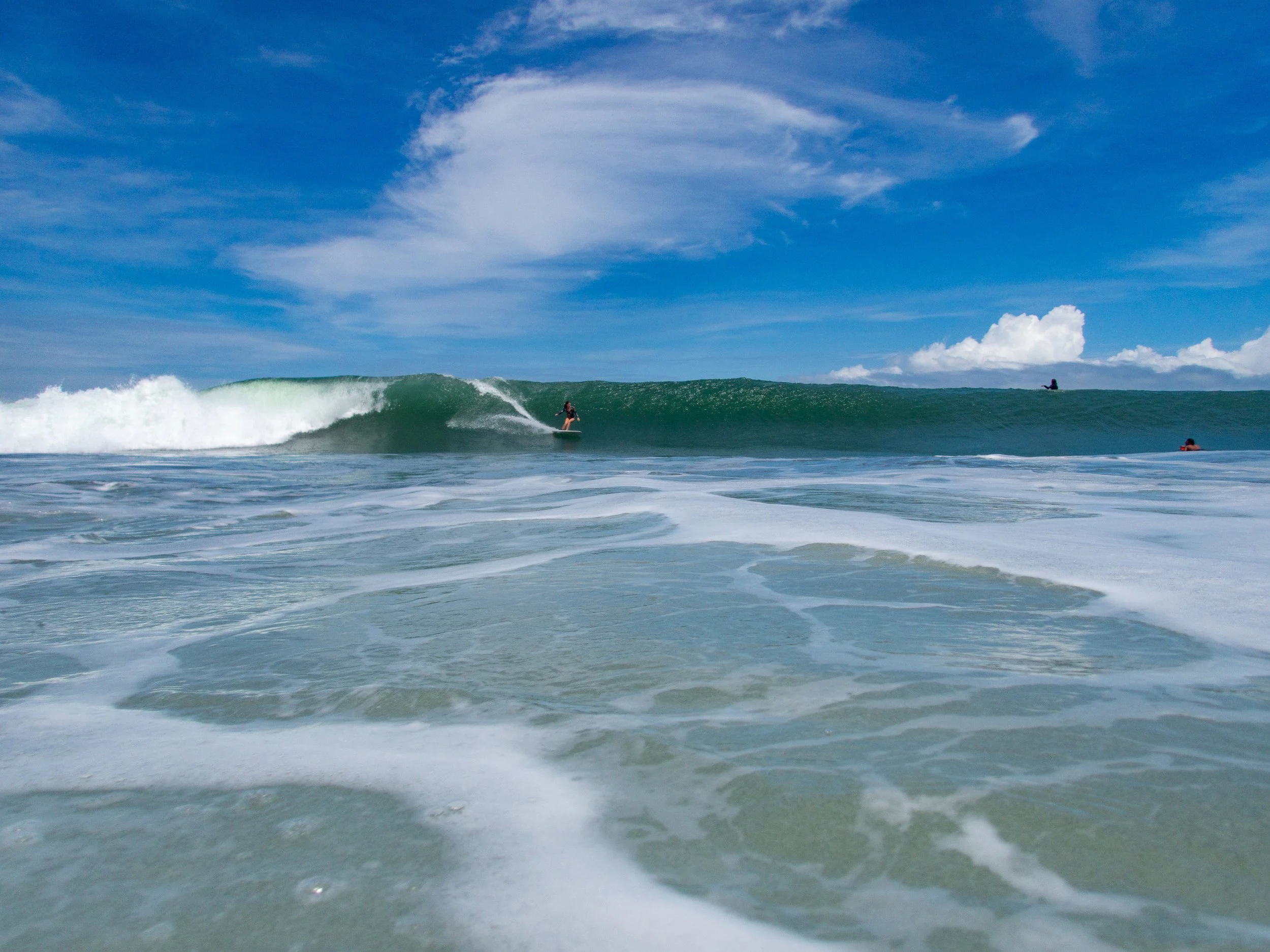 Surfer riding a large wave in the ocean under a blue sky