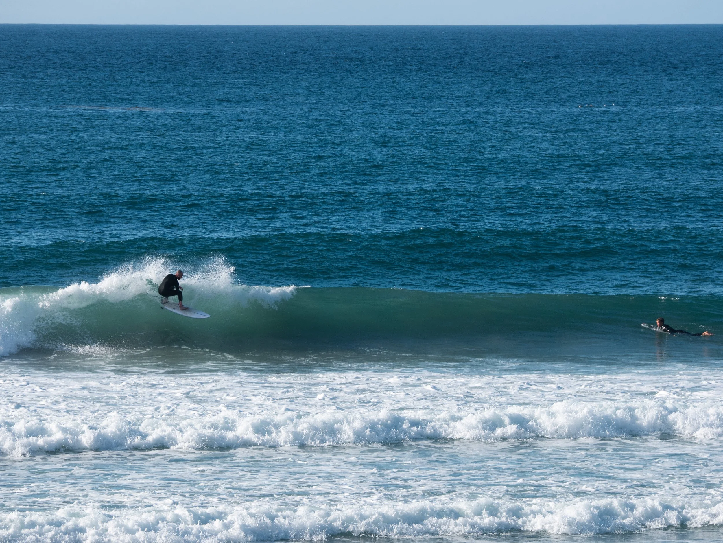 A person surfing on a wave in the ocean with another person swimming nearby.