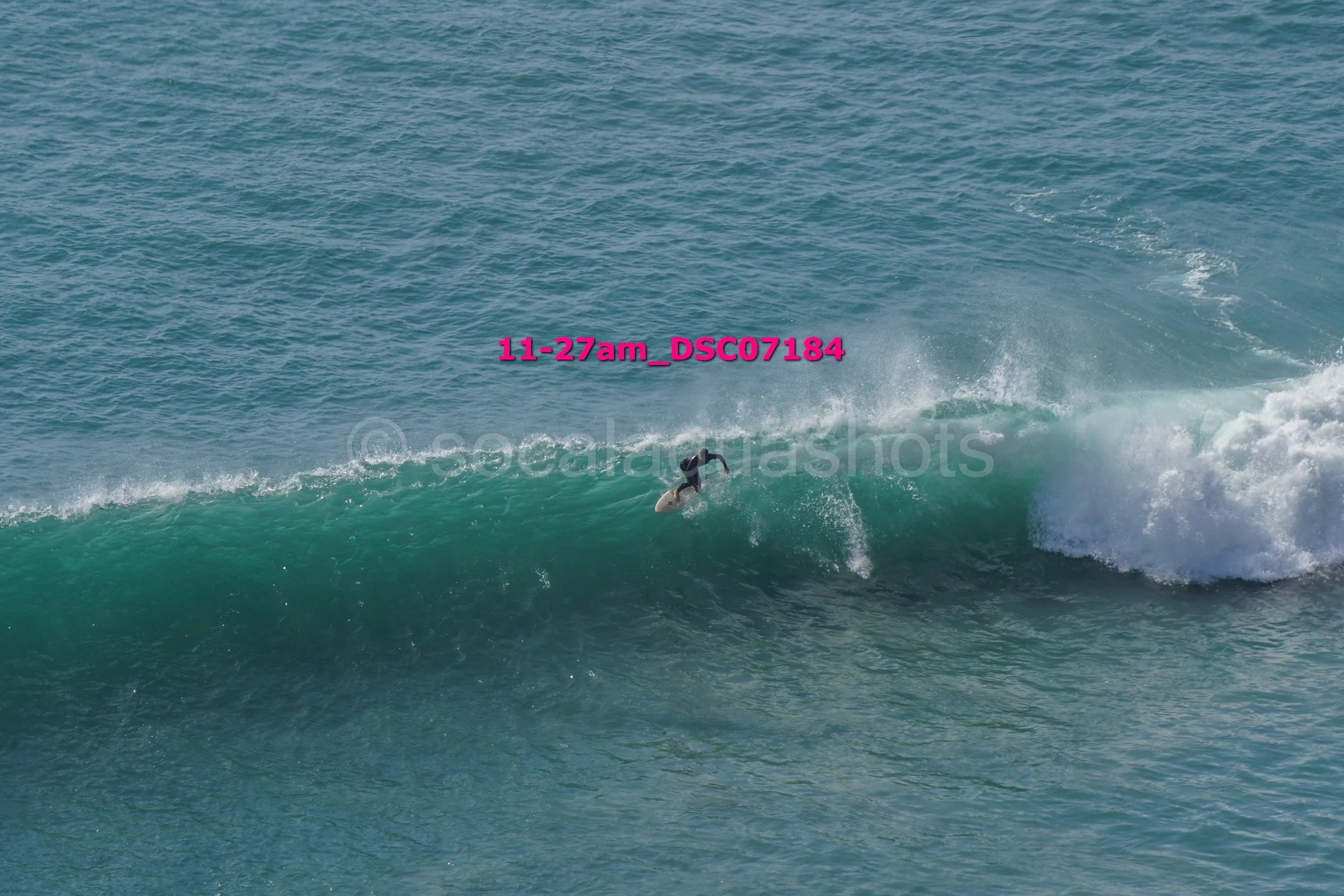 A person surfing on a wave in the ocean with visible spray and turquoise water.