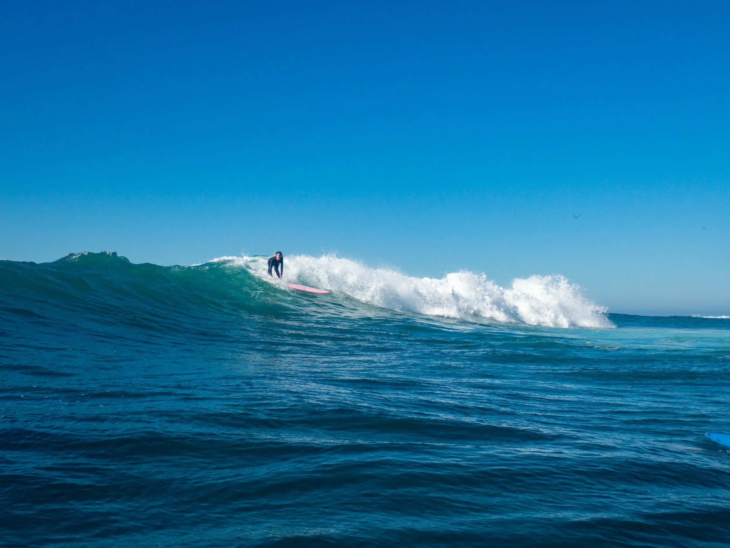 A person surfing on a wave in the ocean during daytime with a clear blue sky.