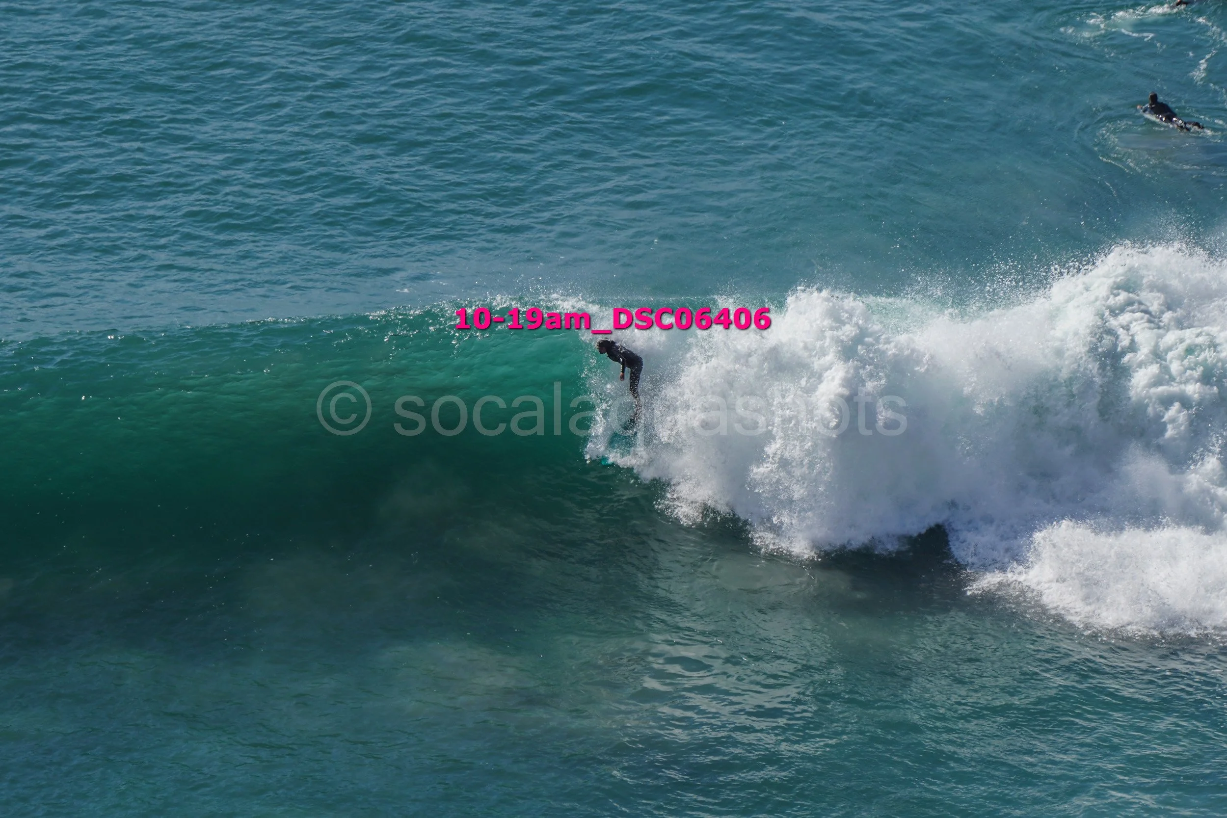 A person surfing on a large wave in the ocean with another surfer paddling nearby.