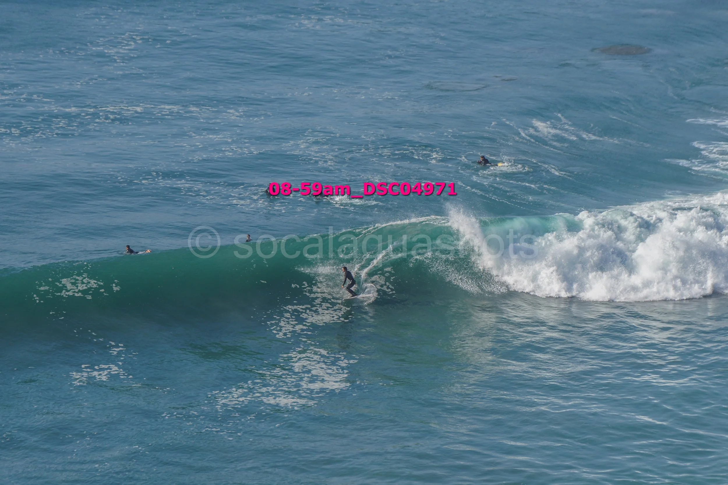 Person surfing on a wave in the ocean with two other surfers in the background.