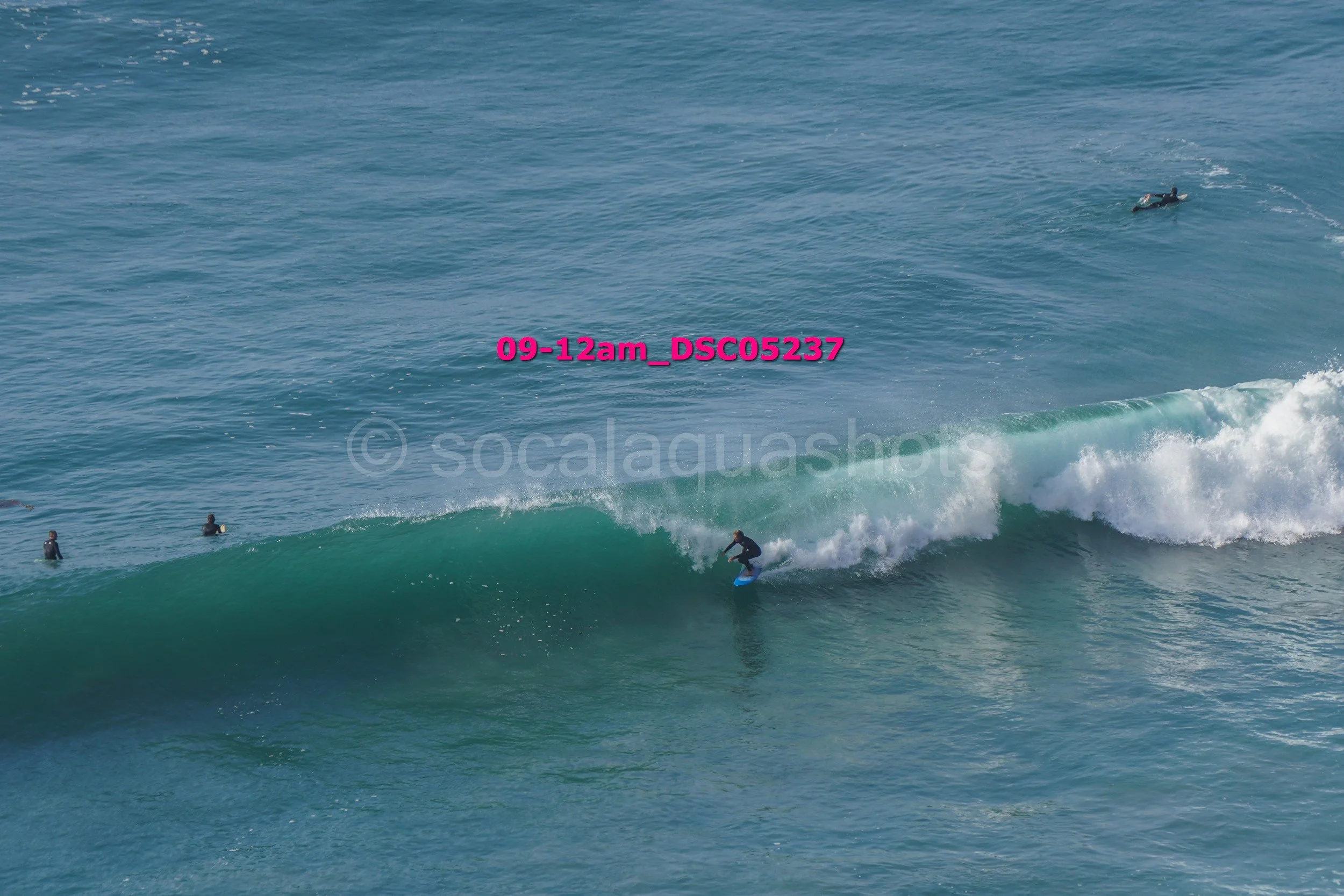 Surfer riding a wave in the ocean with three people in the water nearby and another person on a surfboard in the distance.