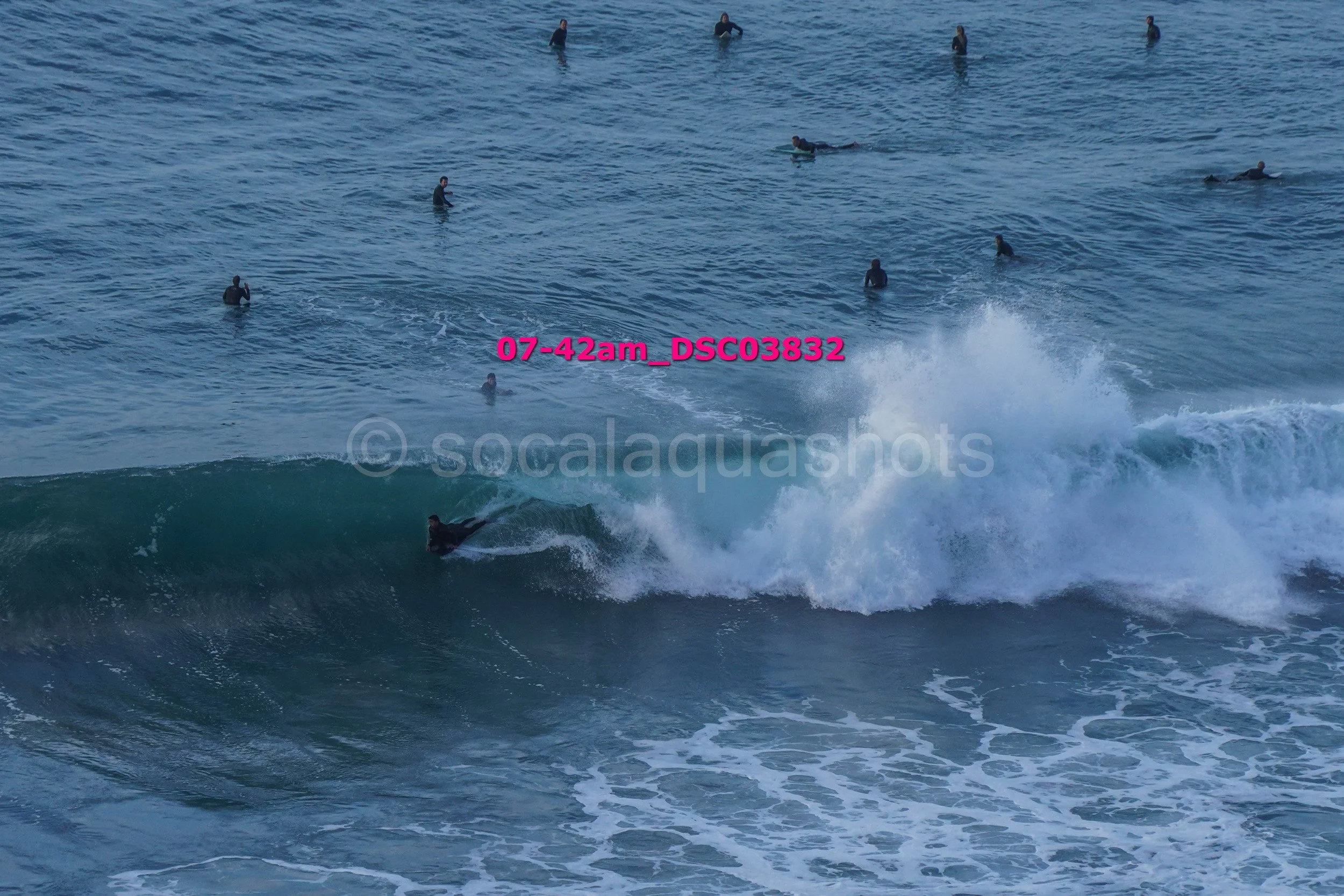 A surfer riding a wave in the ocean with several other people swimming and surfing in the background.